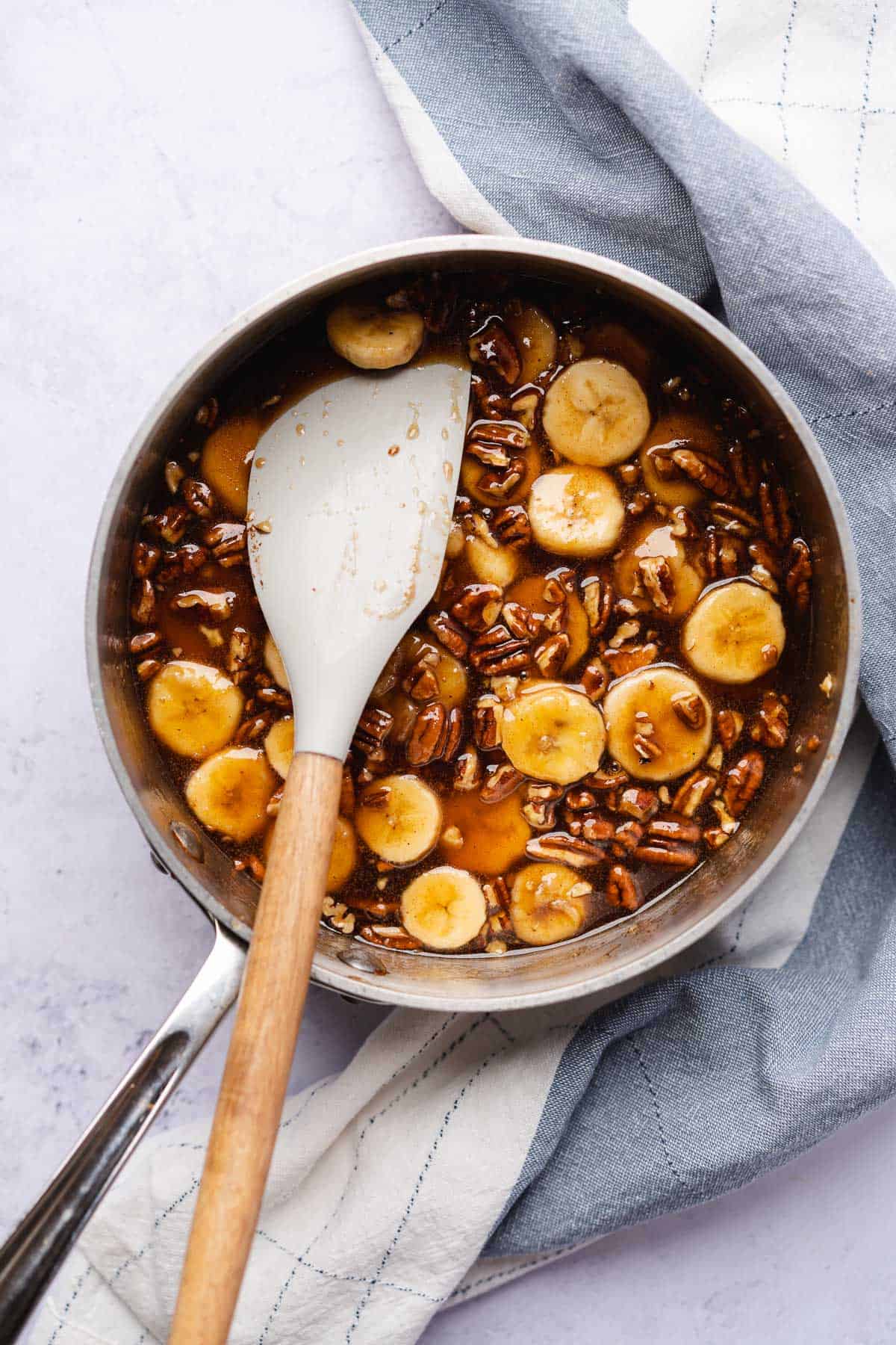 saucy rum banana topping for bananas foster topping in a sauce pan with a rubber a spatula