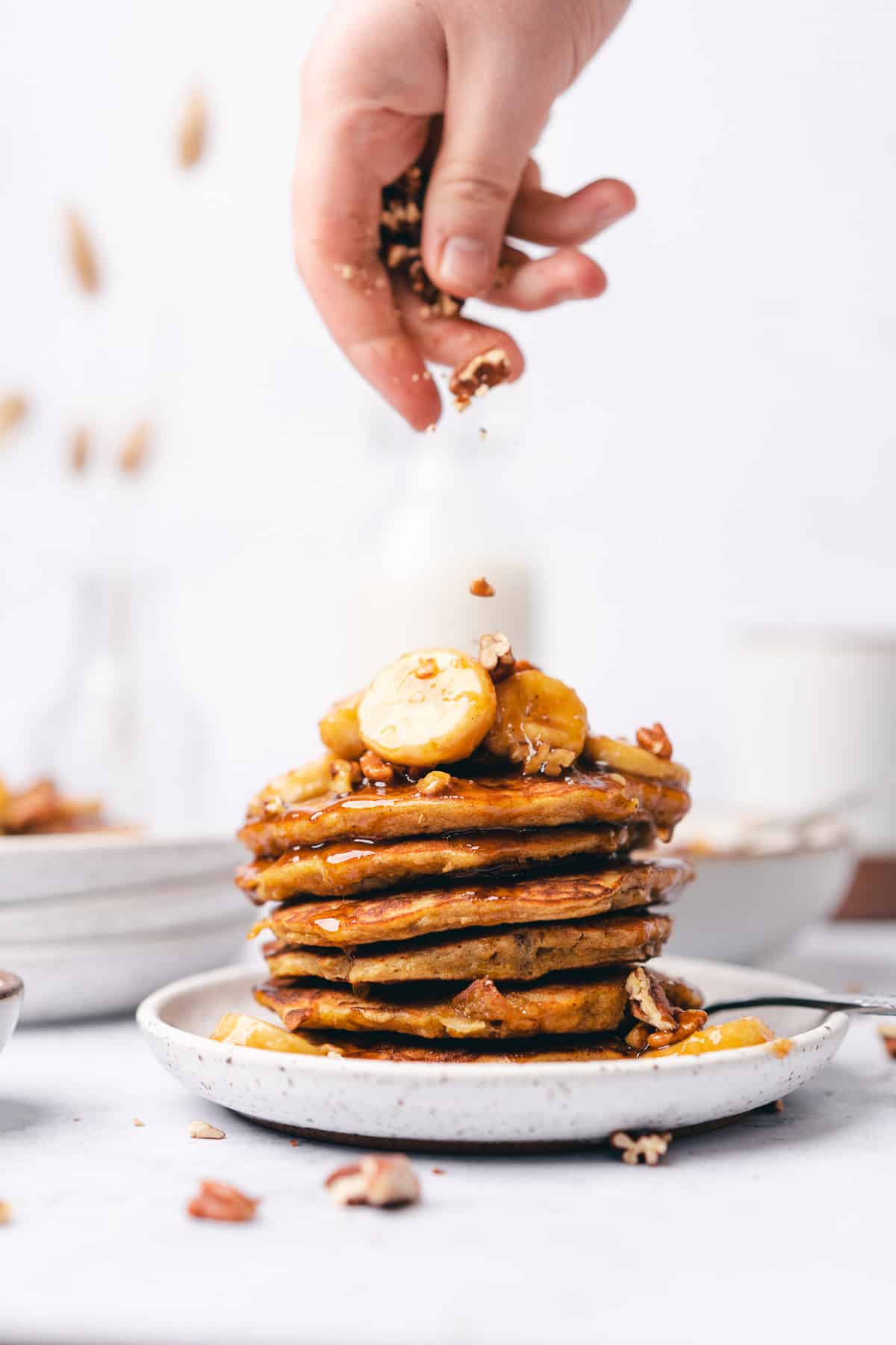 hand sprinkling pecans on top of a stack of pancakes