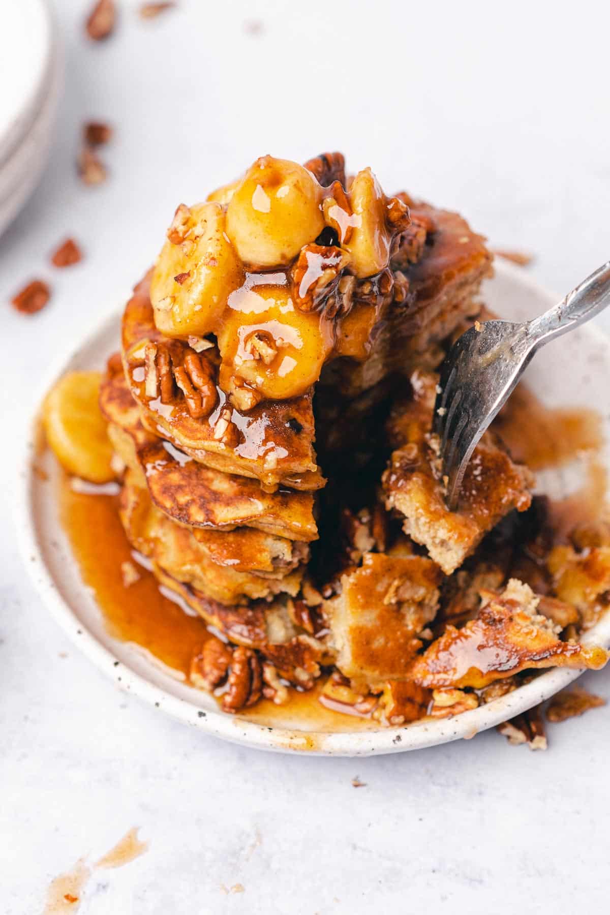 stack of bananas foster pancakes with a fork taking a bite in the stack