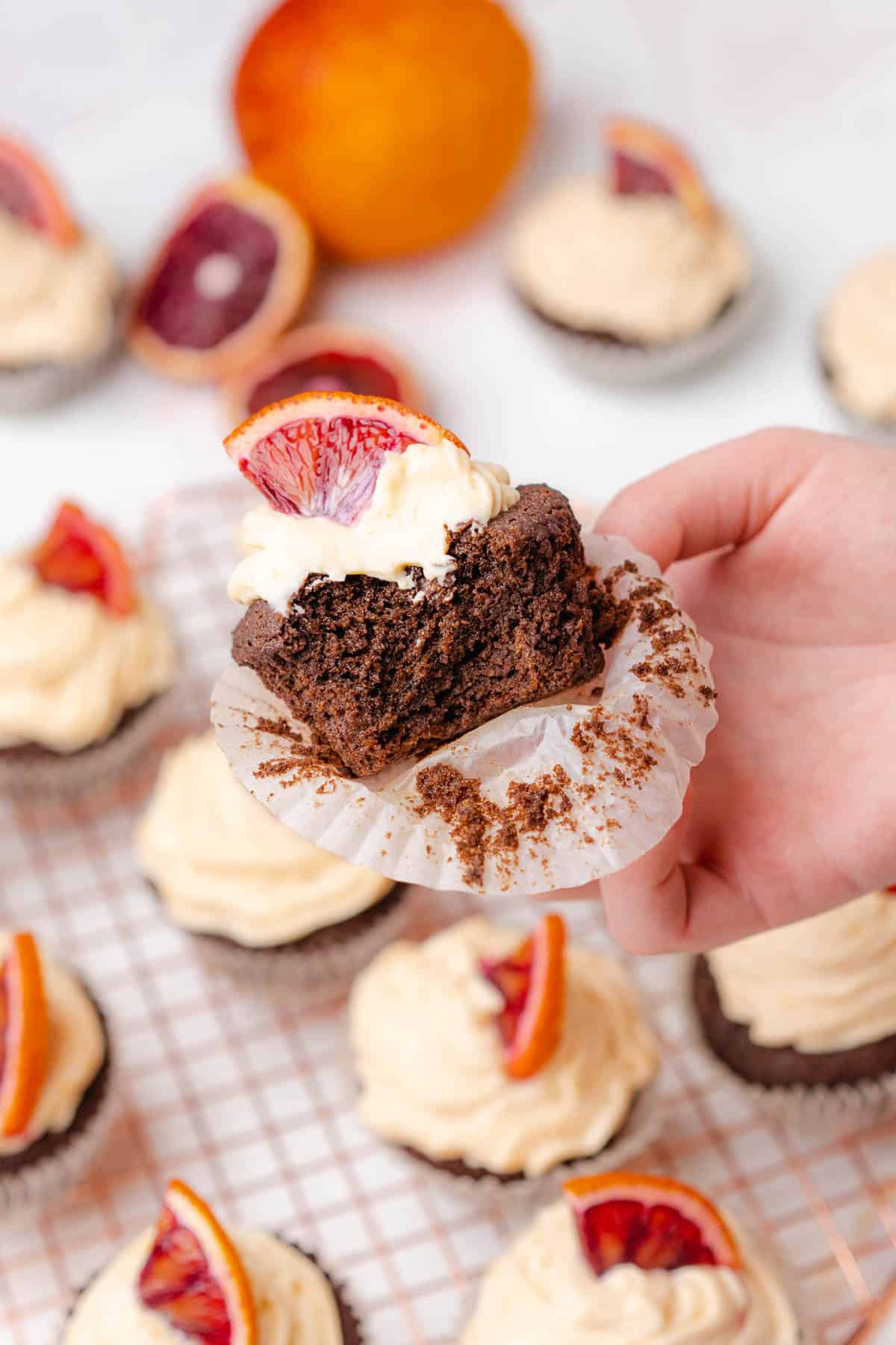 hand holding a chocolate blood orange cupcake with a bite taken out open to show off the center