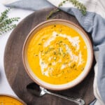 cauliflower and pumpkin soup in a ceramic bowl with a brown rim, fresh thyme and a drizzle of heavy cream