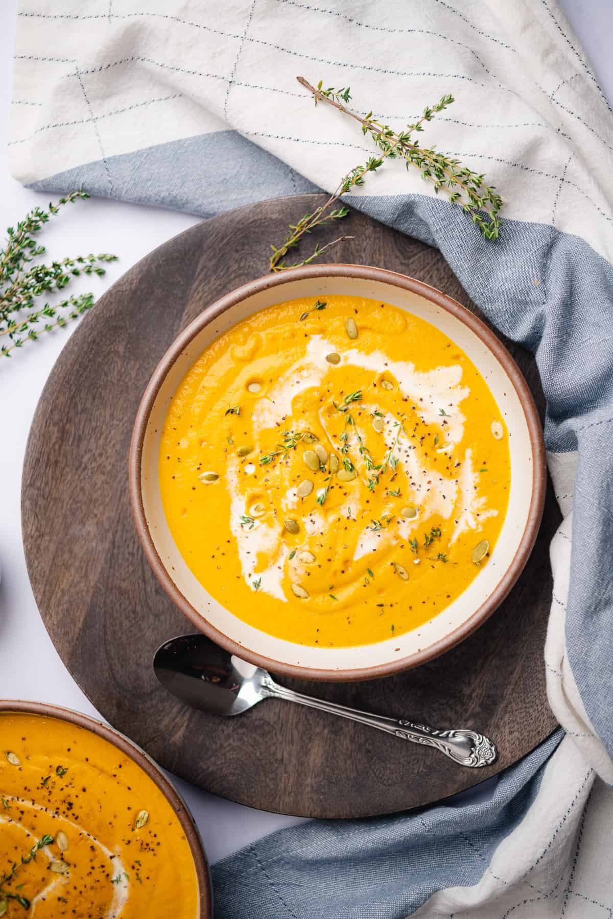 cauliflower and pumpkin soup in a ceramic bowl with a brown rim, fresh thyme and a drizzle of heavy cream