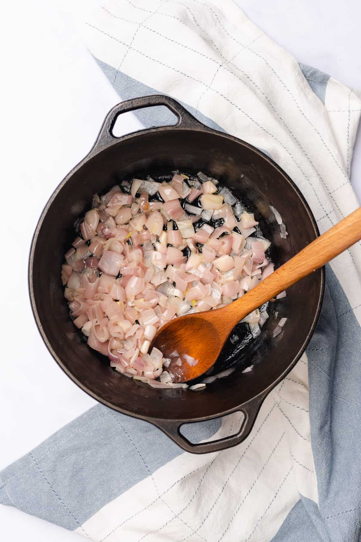 cooking down shallots in a cast iron dutch oven with a wooden spoon