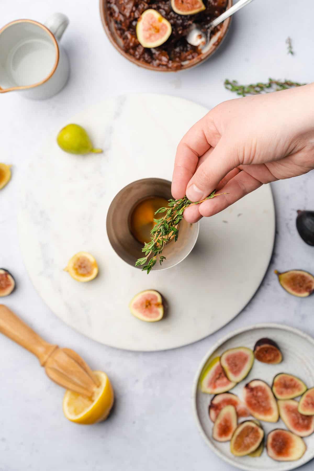 adding fresh thyme to a cocktail shaker surrounded by fresh figs 