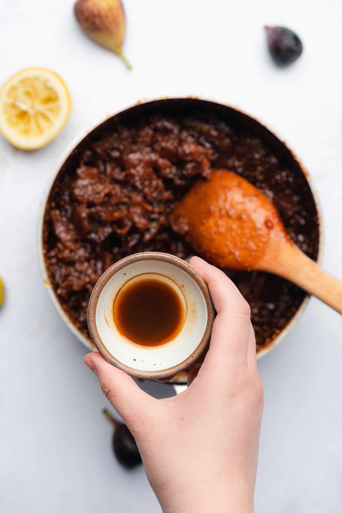 fig spread with a hand hovering over a saucepan with vanilla extract