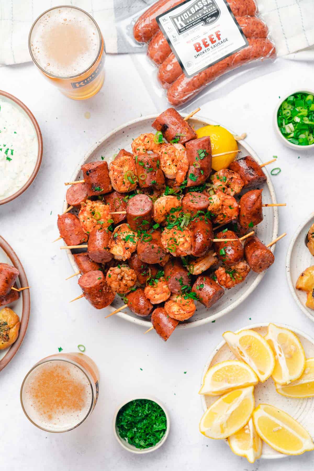 flat lay of kiolbassa smoked meats grilled smoked sausage and shrimp skewers with a great spread for a tailgate or bbq