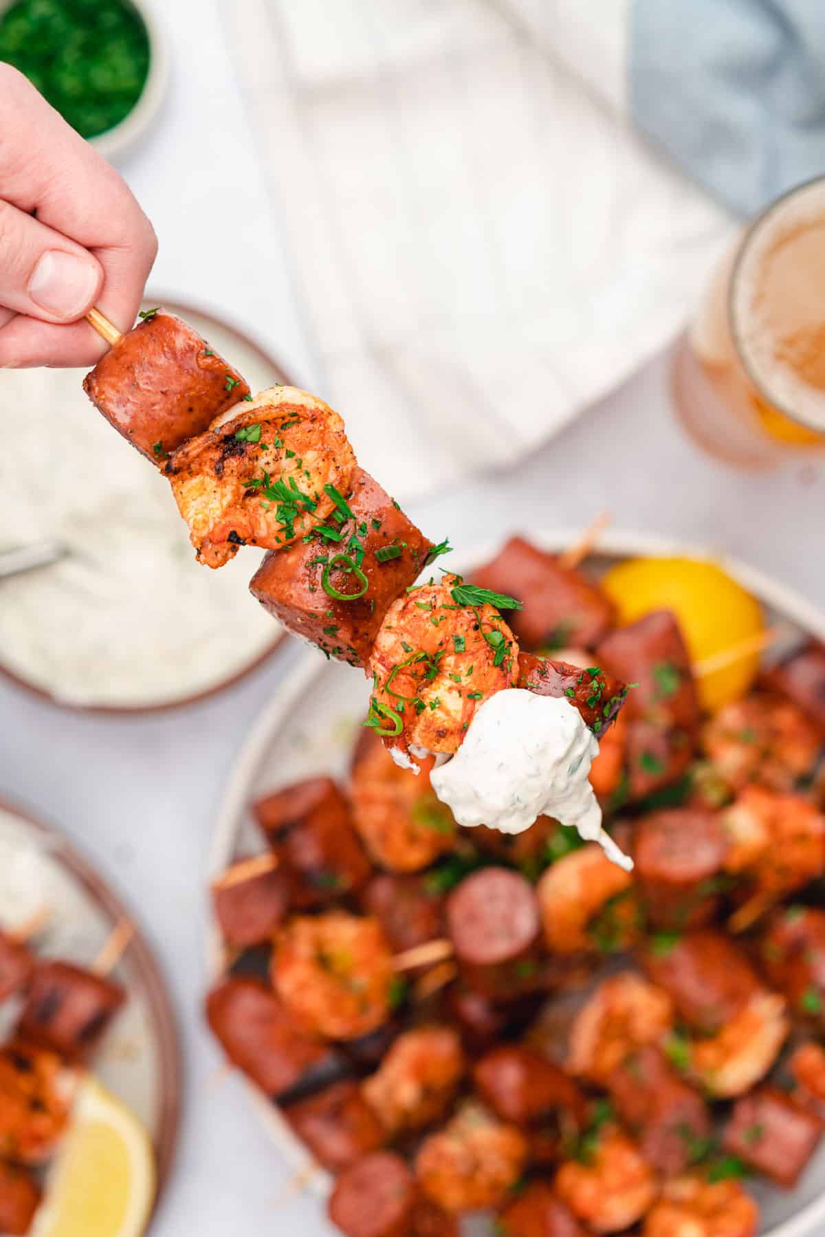 grilled smoked sausage and shrimp skewer hand held with a creamy dipping sauce at the tip
