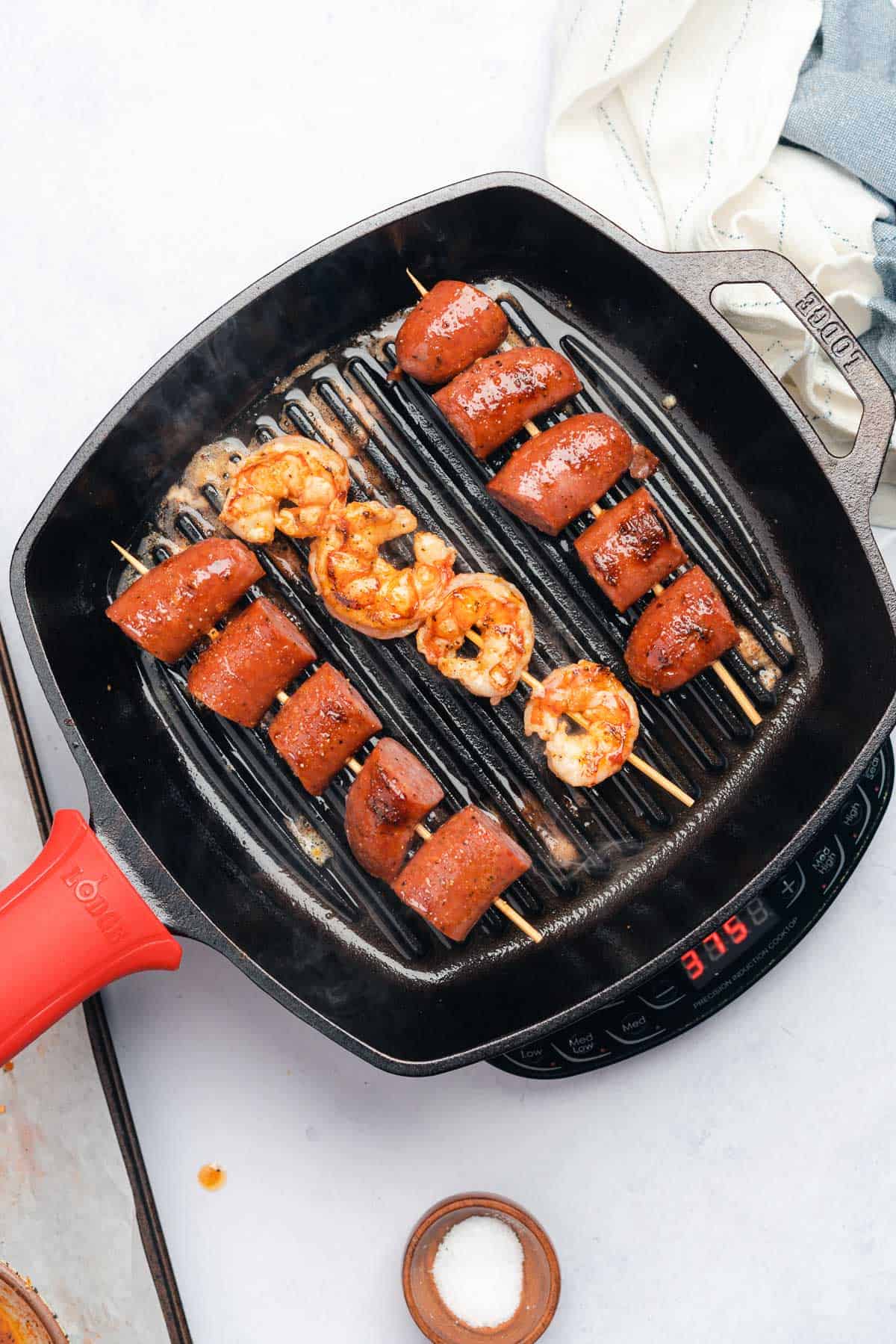 grilling shrimp and sausage skewers on a cast iron griddle pan 