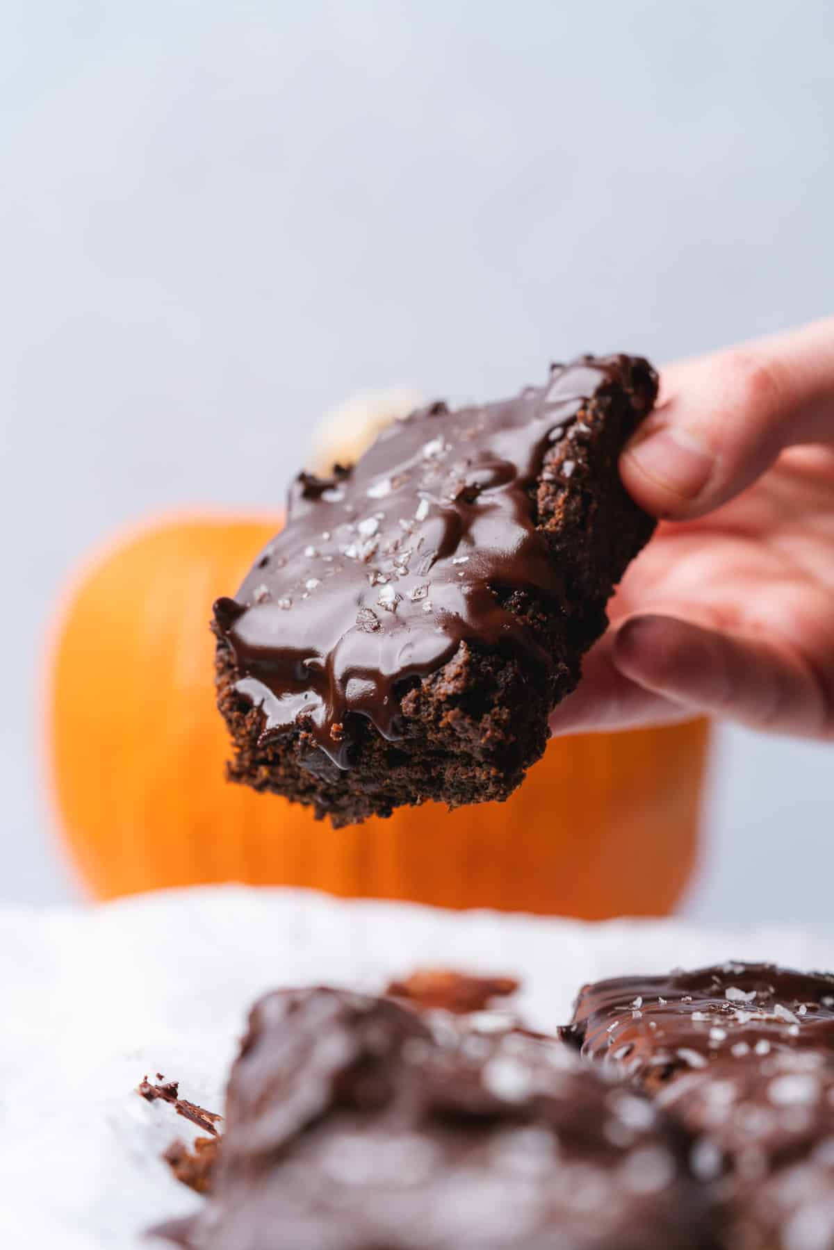 hand held chocolate keto pumpkin brownie with a pumpkin in the background