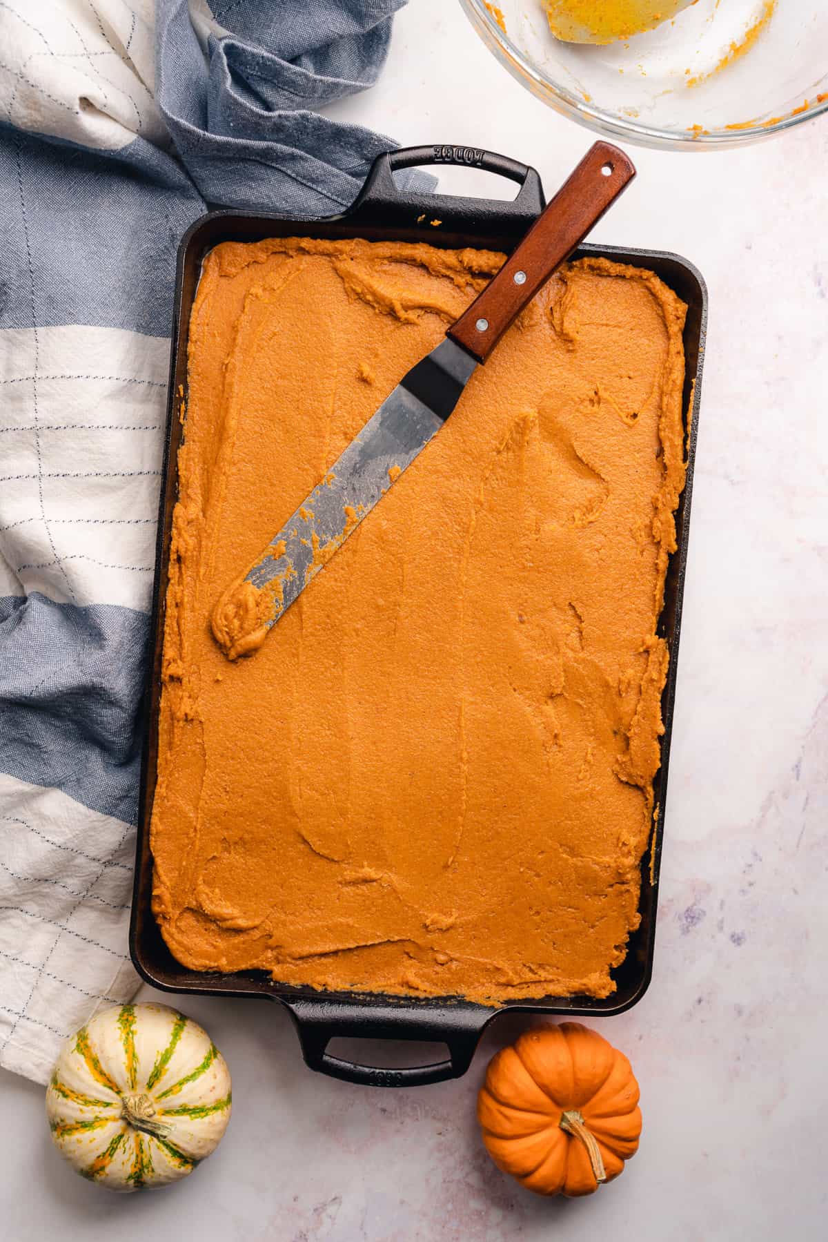 pumpkin bars spread into a cast iron baking pan with a angled spatula overtop