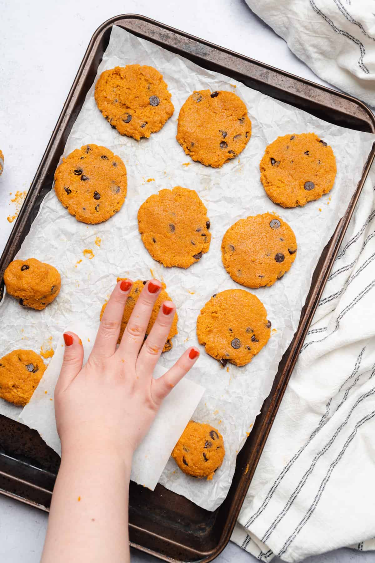 hand pressing down pumpkin chocolate chip cookies onto a baking sheet