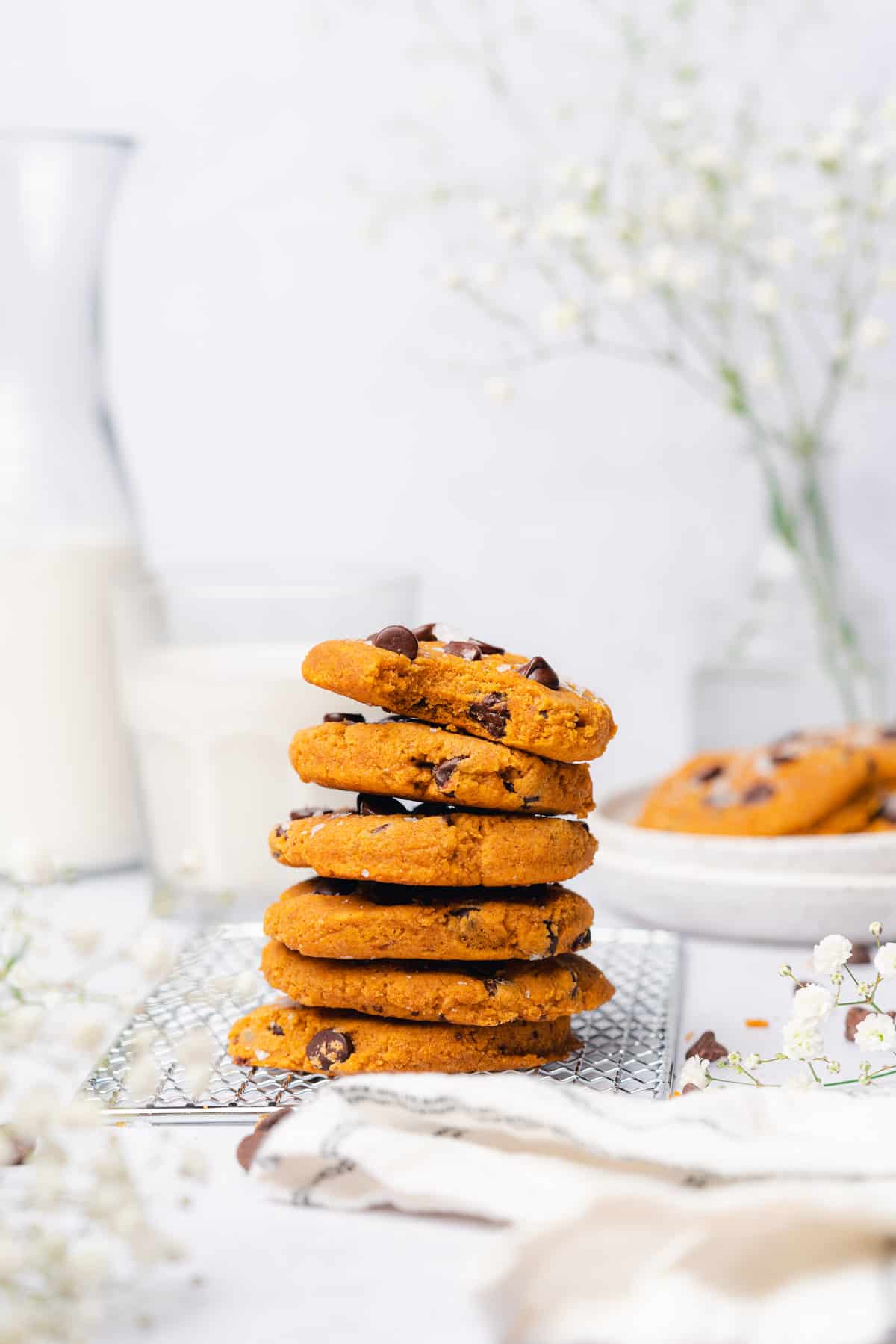 stack of gorgeous pumpkin chocolate chip cookies with milk and baby's breath flowers in the background