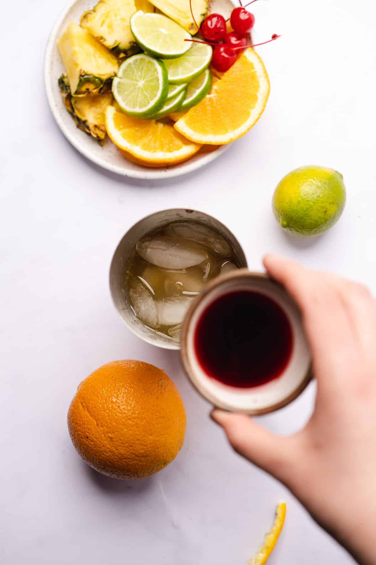 hand holding a small cup of blackberry liqueur to a cocktail shaker