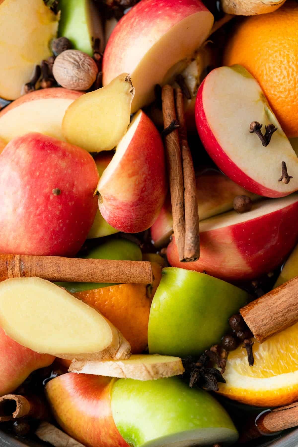 close up shot of cut up apples, orange and various cloves and cinnamon sticks 