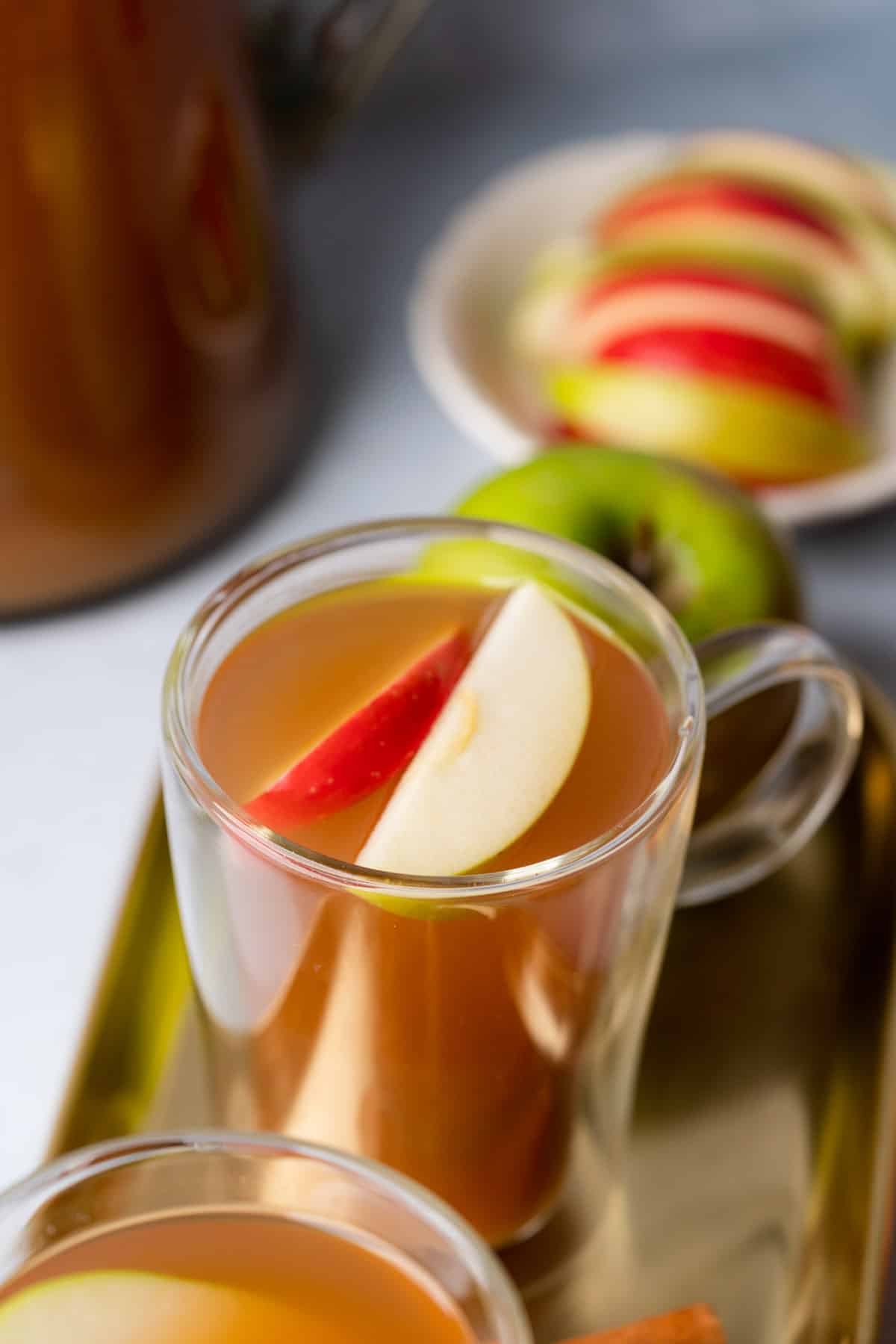 close up shot of two clear glass mugs with sugar free apple cider and topped with apple slices
