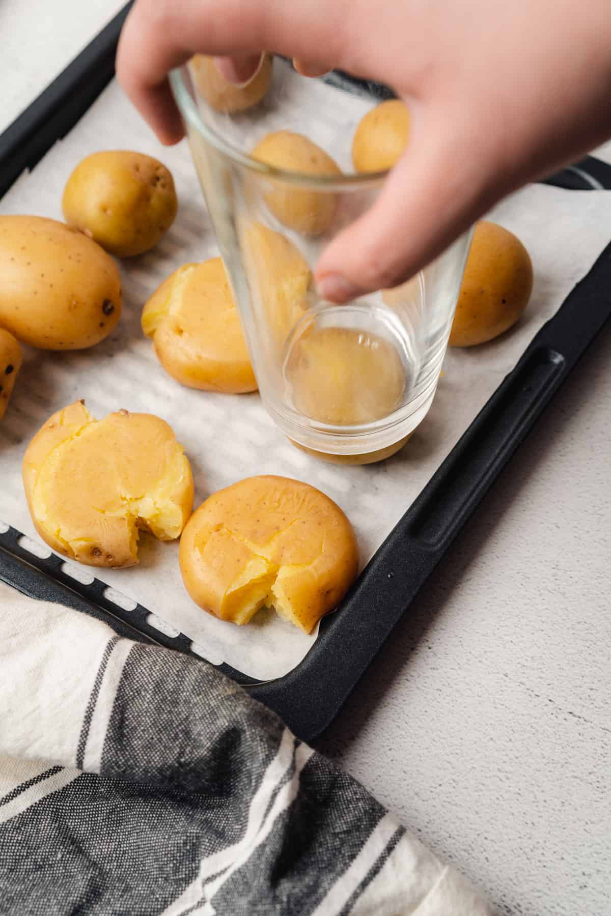 hand using a glass to smash golden baby potatoes 