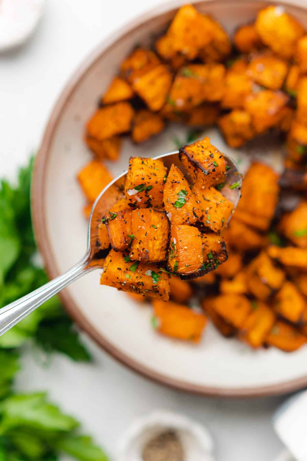 air fryer sweet potato cubes on a spoon seasoned well and garnished with fresh parsley