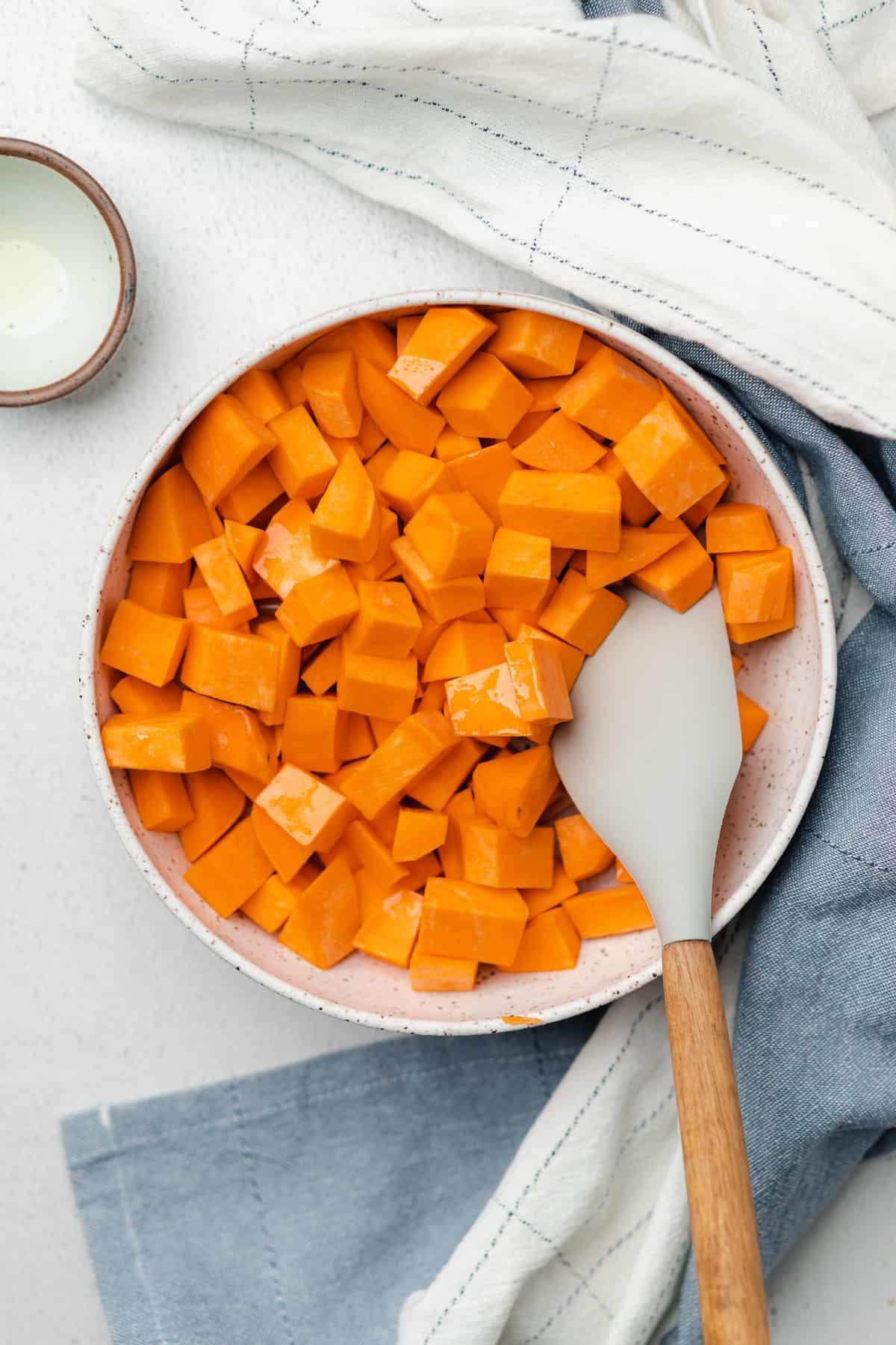 sweet potato cubes in a ceramic bowl with avocado oil and rubber spatula 