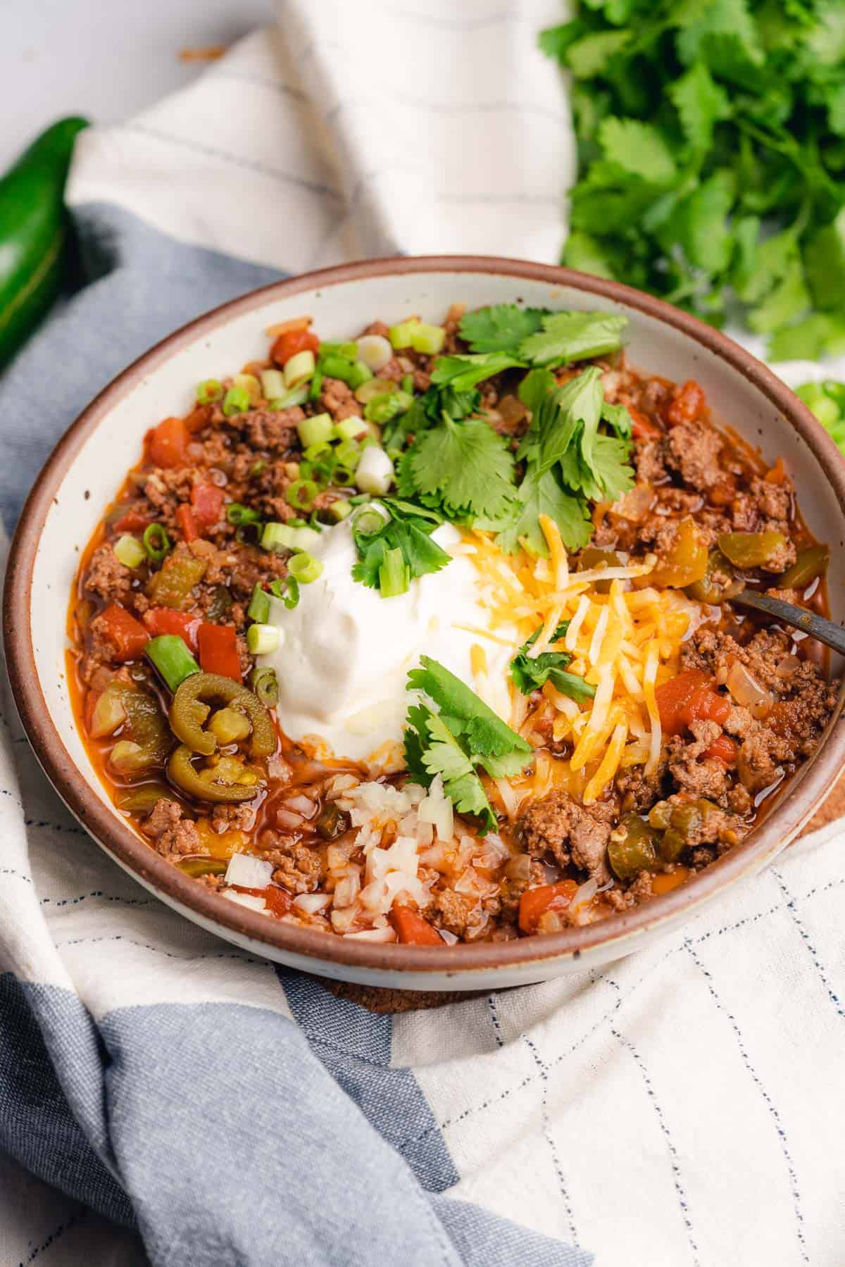 large bowl of chili with cheese, sour cream, green onions, cilantro and pickled jalapeños