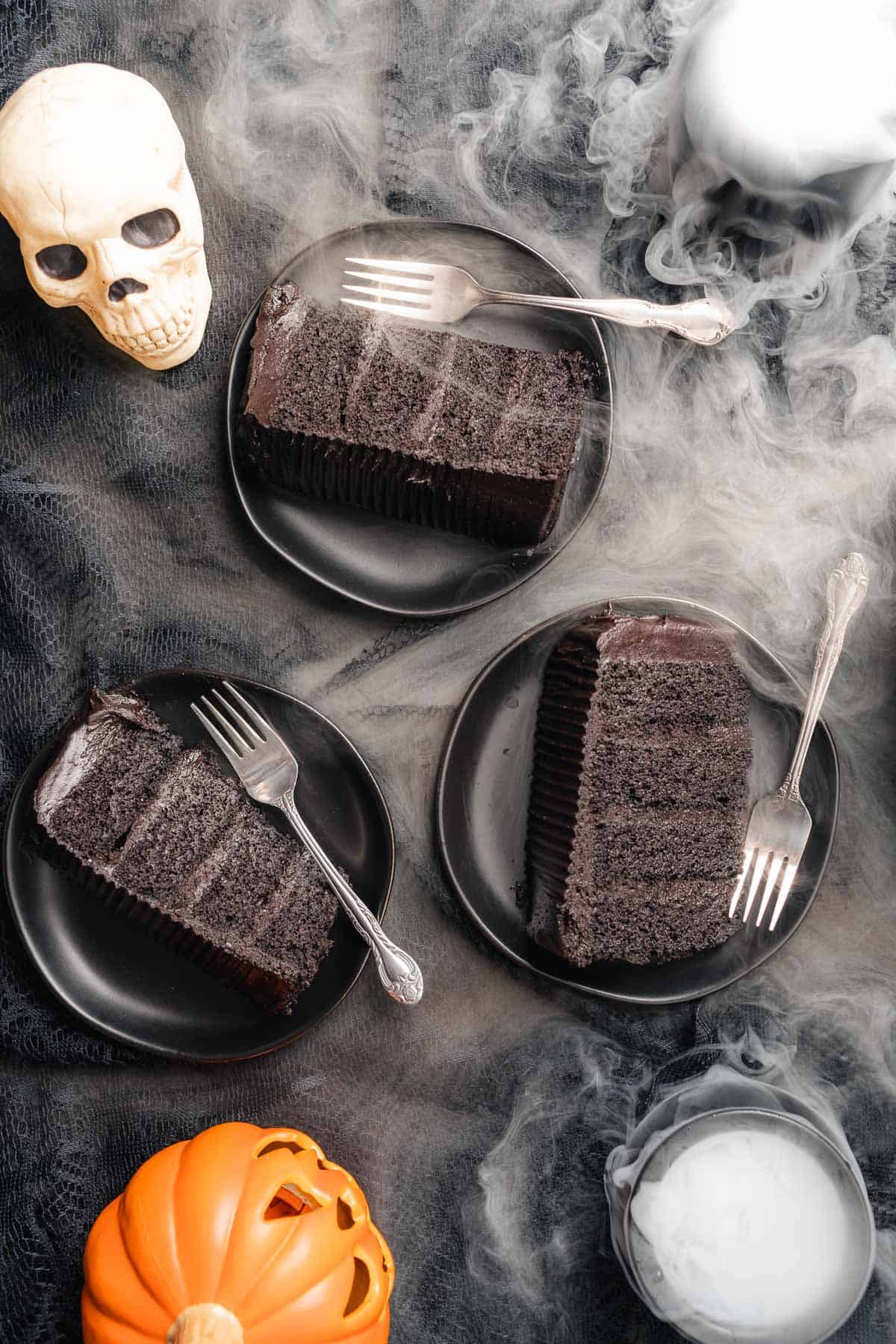flat lay shot of black velvet cake slices on black plates with a skull and dry ice 