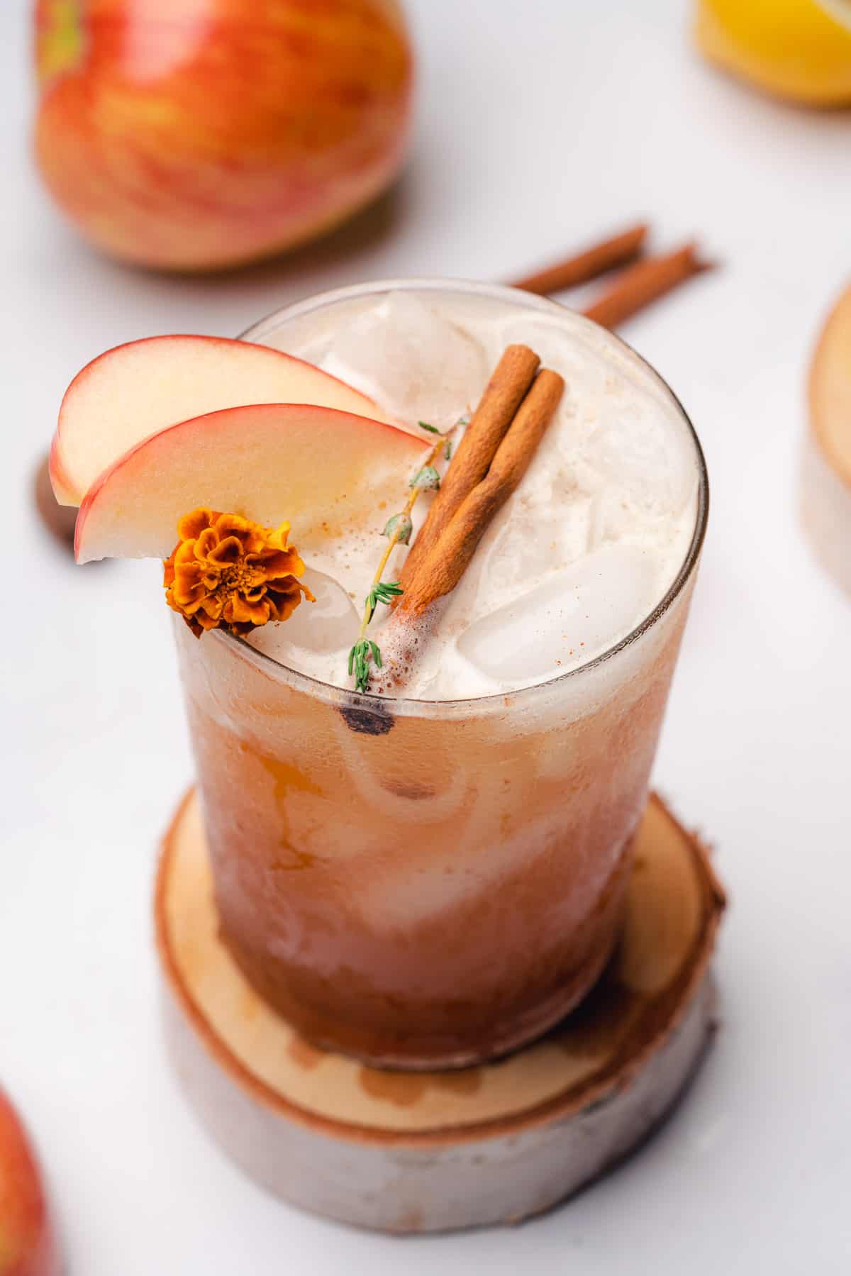 bourbon apple smash garnished with cinnamon sticks, apple slices, thyme, and a marigold flower