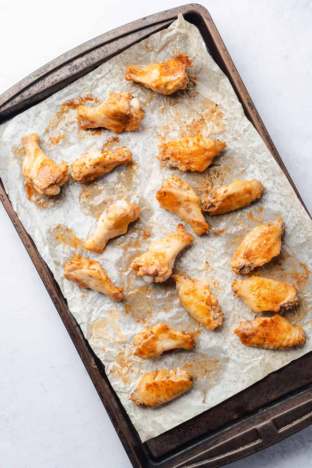 crispy chicken wings on a parchment lined baking sheet flipped halfway through to show a browned underside 