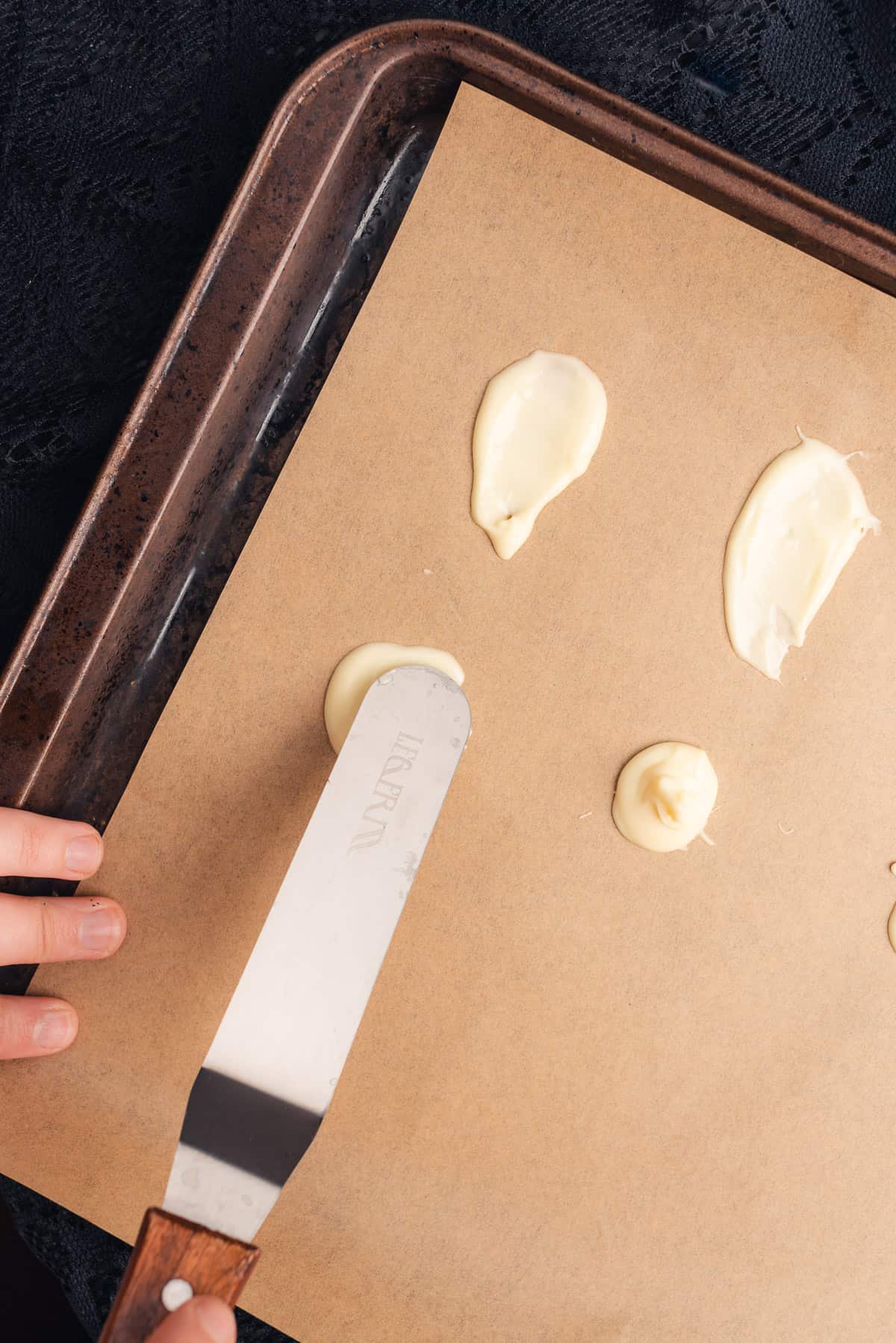 using an angled spatula to make a white chocolate ghost shape on parchment 
