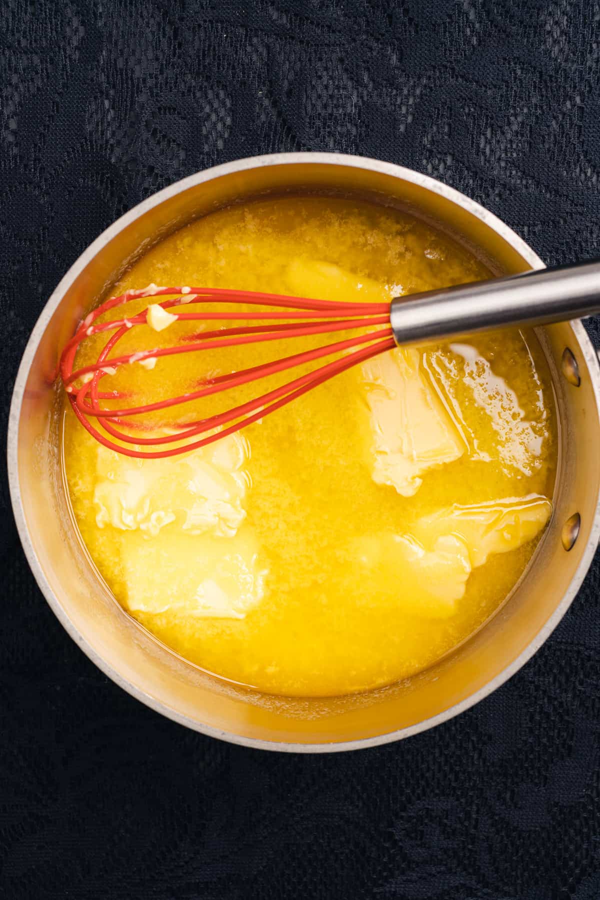 melting butter in a saucepan with a red silicone whisk