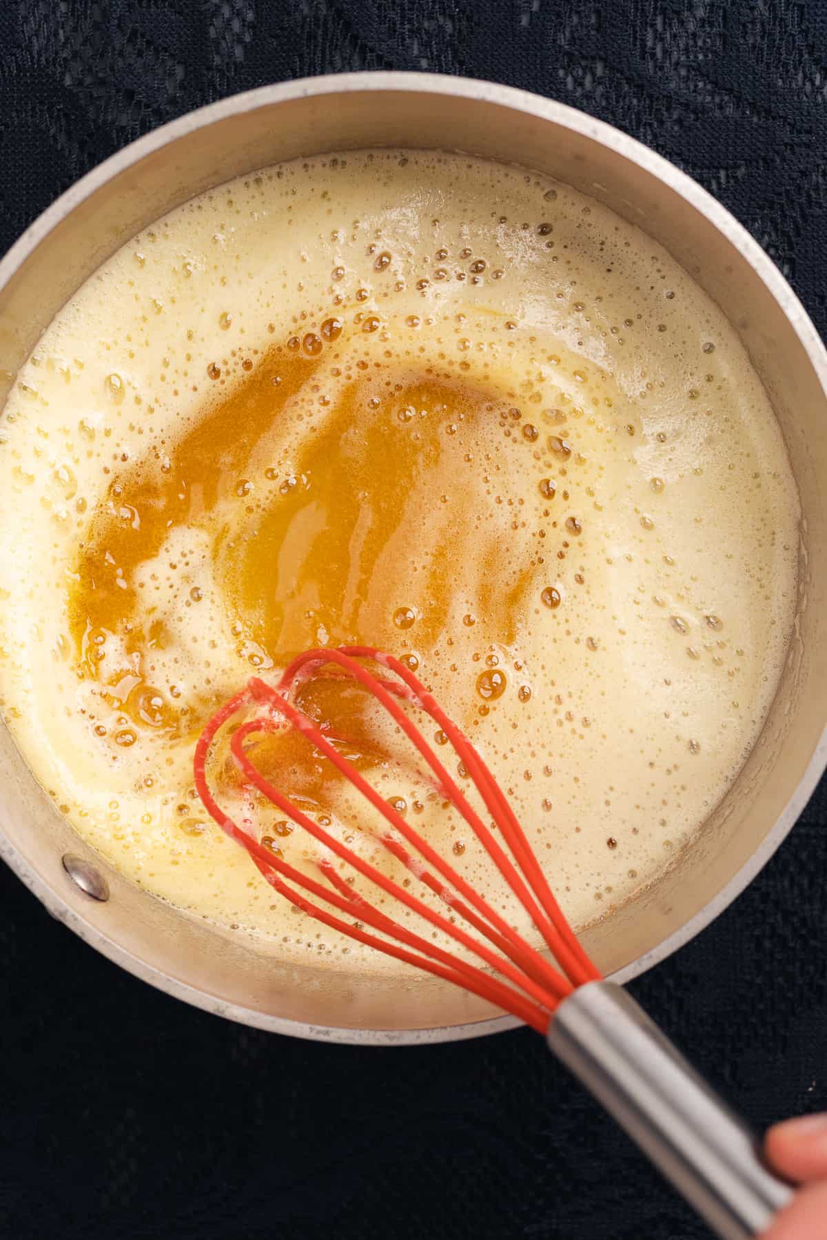 whisking brown butter in a saucepan with a red silicone whisk