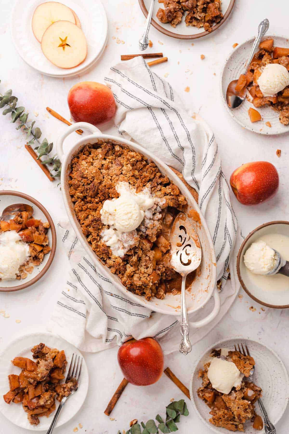 flat lay of a sugar free apple crisp recipe with apples, and plates of apple crisp surrounding the baking dish