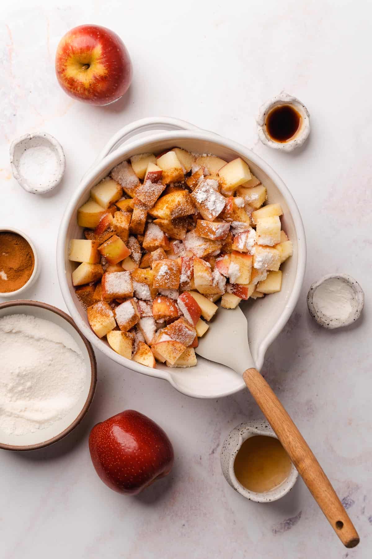 mixing apples together in a bowl with cinnamon, cornstarch, sweetener, and vanilla