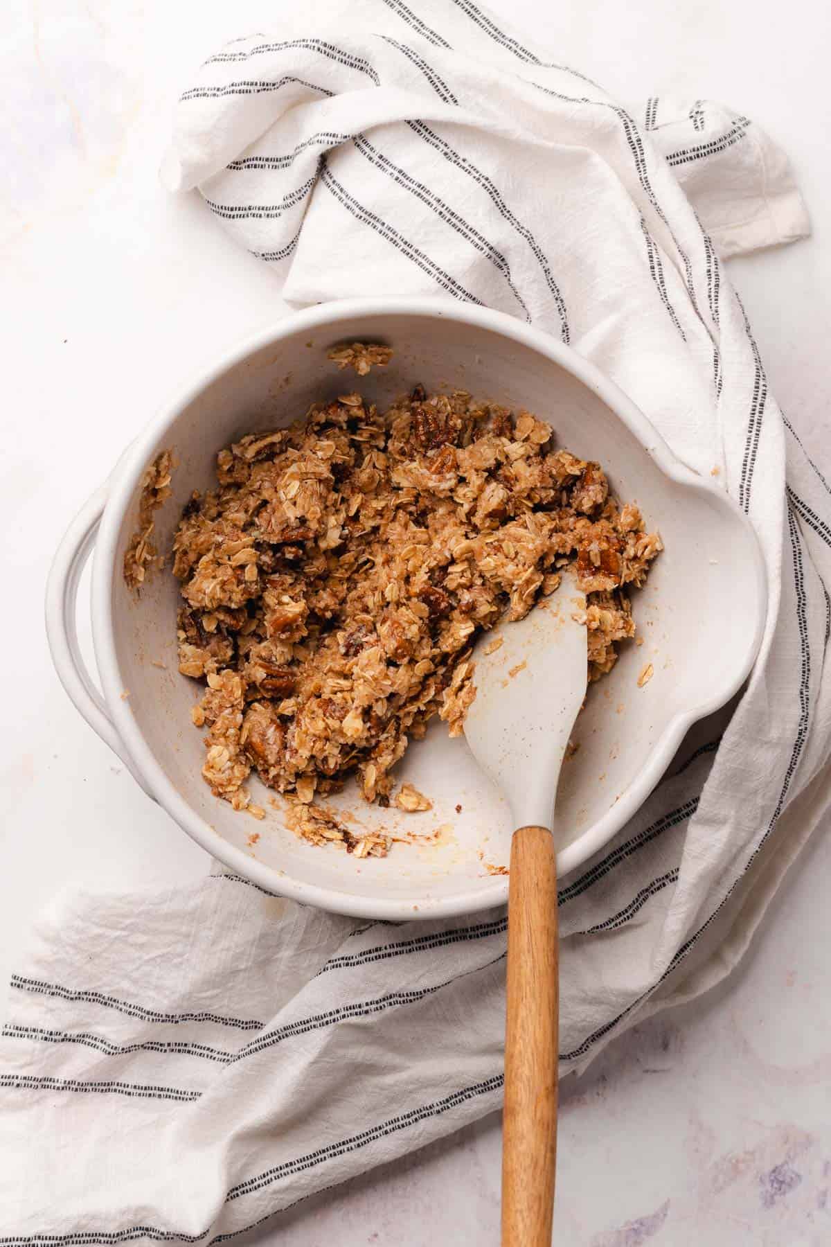 spatula mixing together dry crumble topping ingredients  in a ceramic bowl