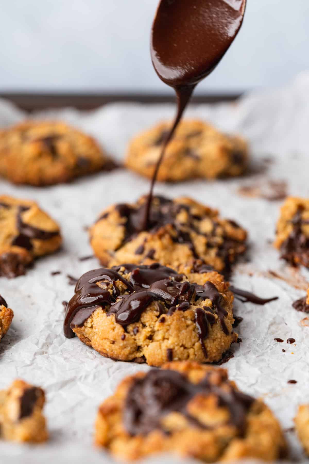 spoonful of chocolate drizzle going on top of a large keto peanut butter chocolate chip cookie