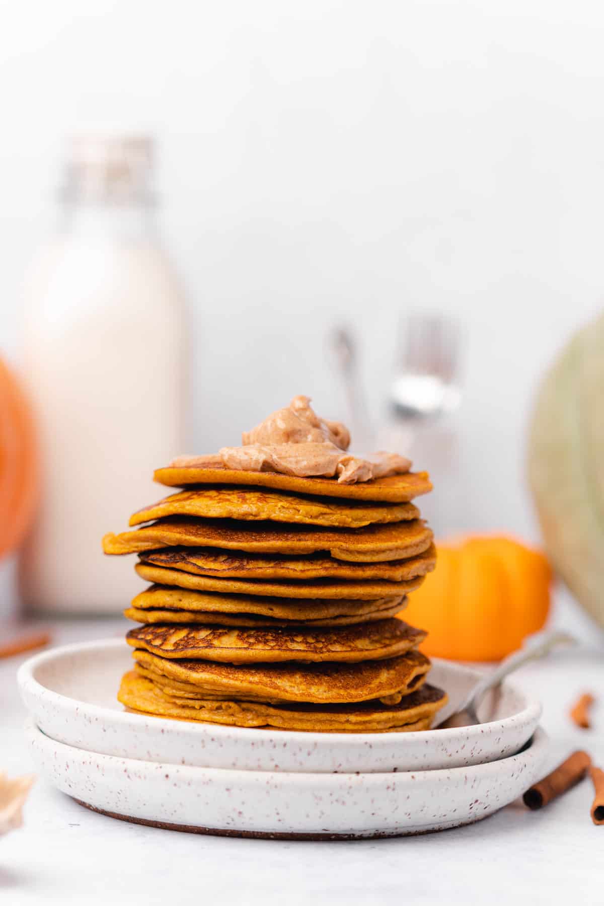 large stack of pumpkin pancakes with a dollop of whipped butter on top and gourds in the background