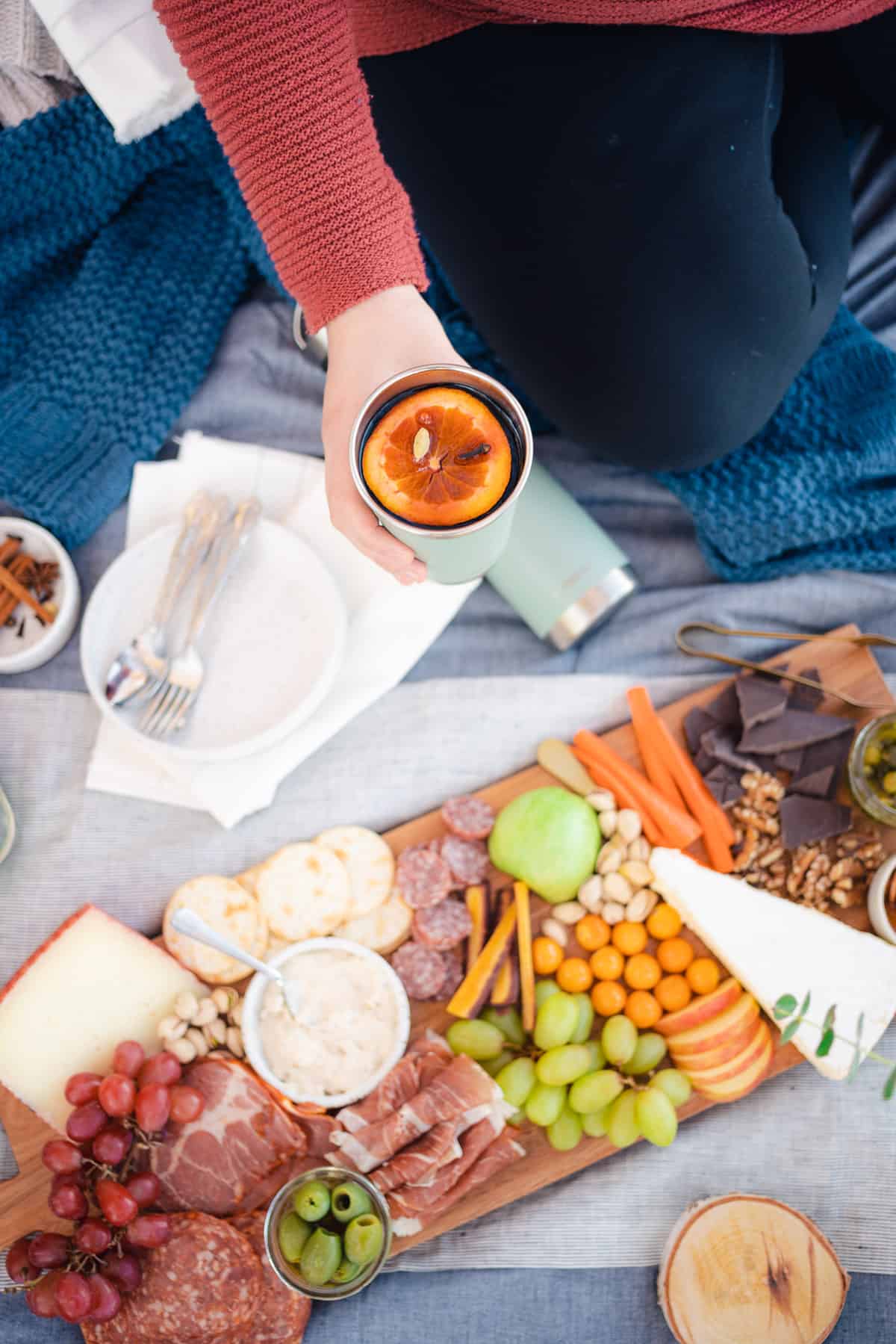flatlay of a fall picnic date setup with a charcuterie board and a girl holding a glass of mulled wine
