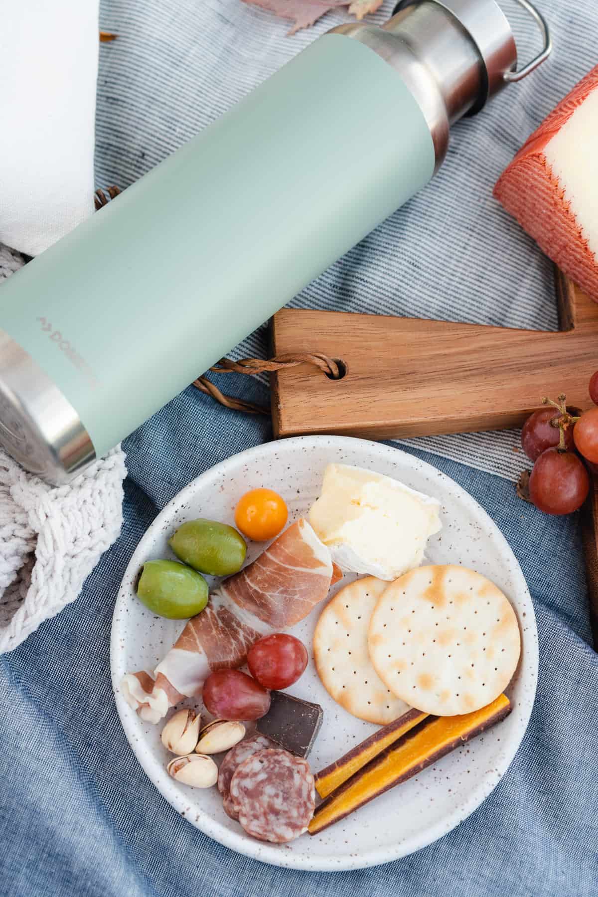 flat lay photo of a ceramic plate with charcuterie food and a metal tumbler bottle filled with mulled wine