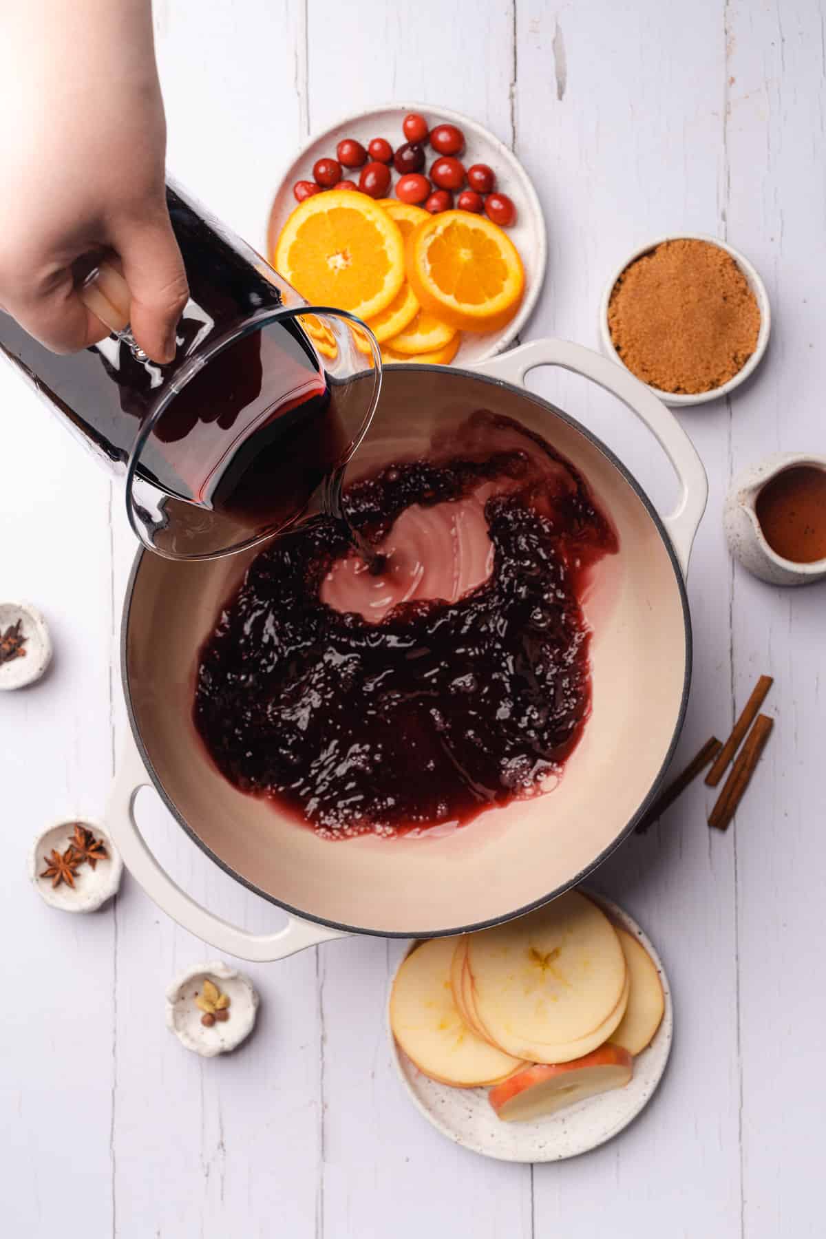 pouring red wine into an enameled dutch oven to make mulled wine
