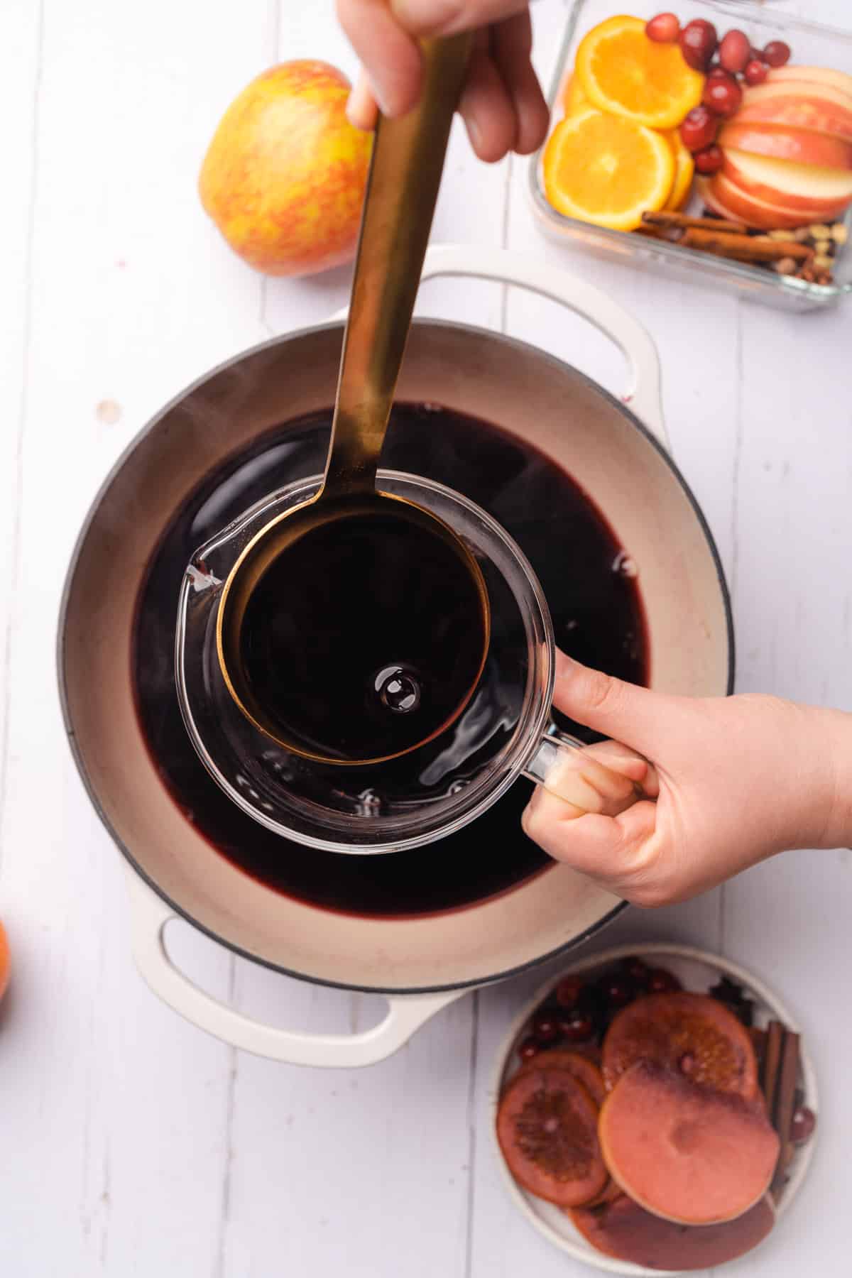ladeling mulled wine into a glass pitcher from a dutch oven