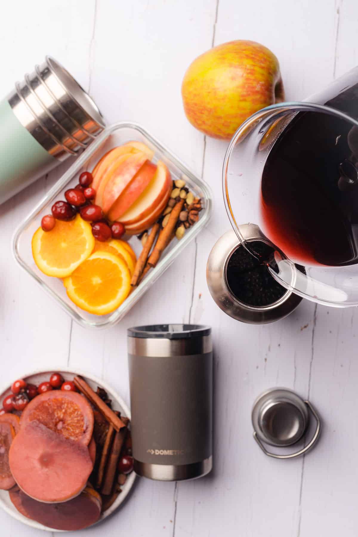 pouring mulled wine into Dometic thermal tumblers to keep warm, surrounded by fresh fruit garnishes and thermal cups