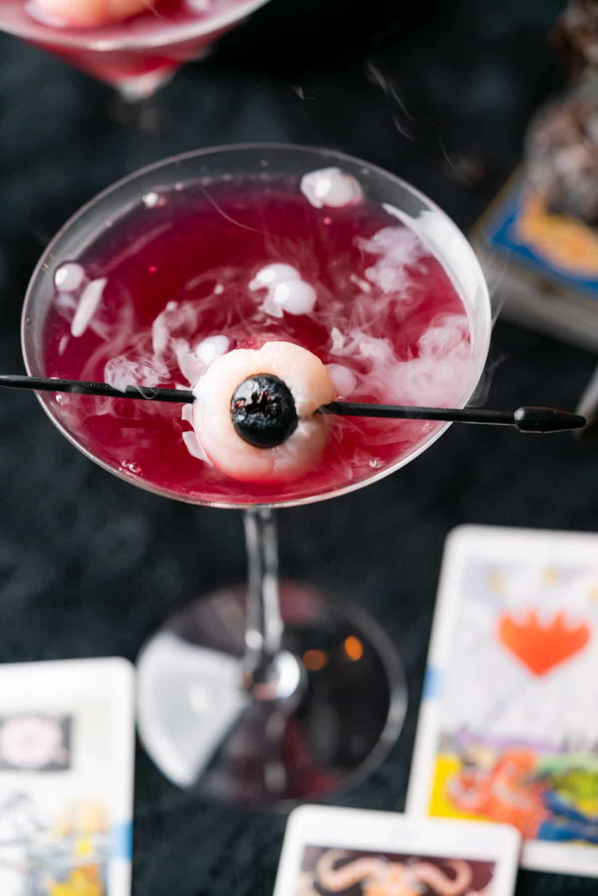 a spooky purple cocktail with tarot cards, dry ice and a lychee eyeball