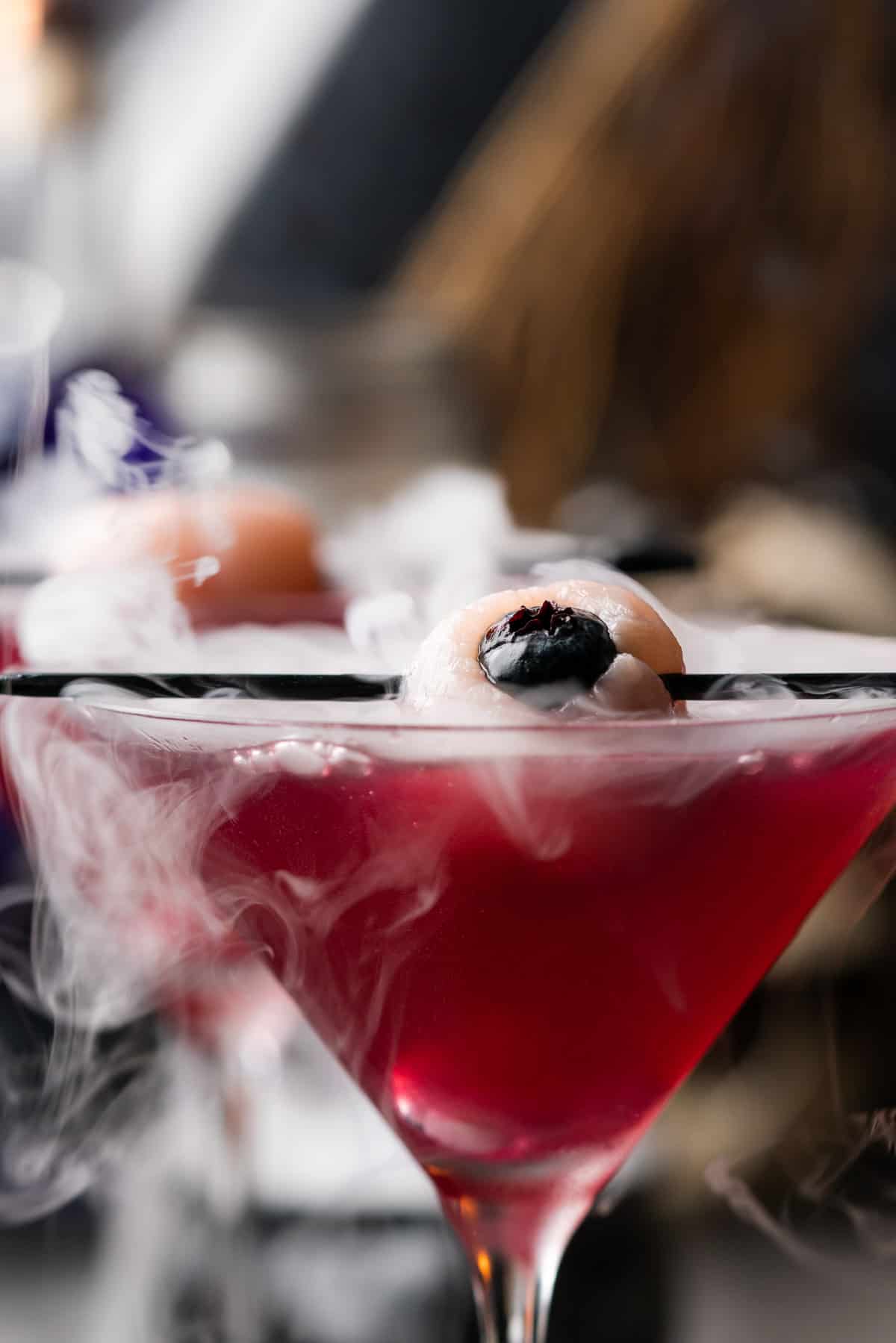 close up shot of a lychee eyeball in a bubbling purple gin cocktail