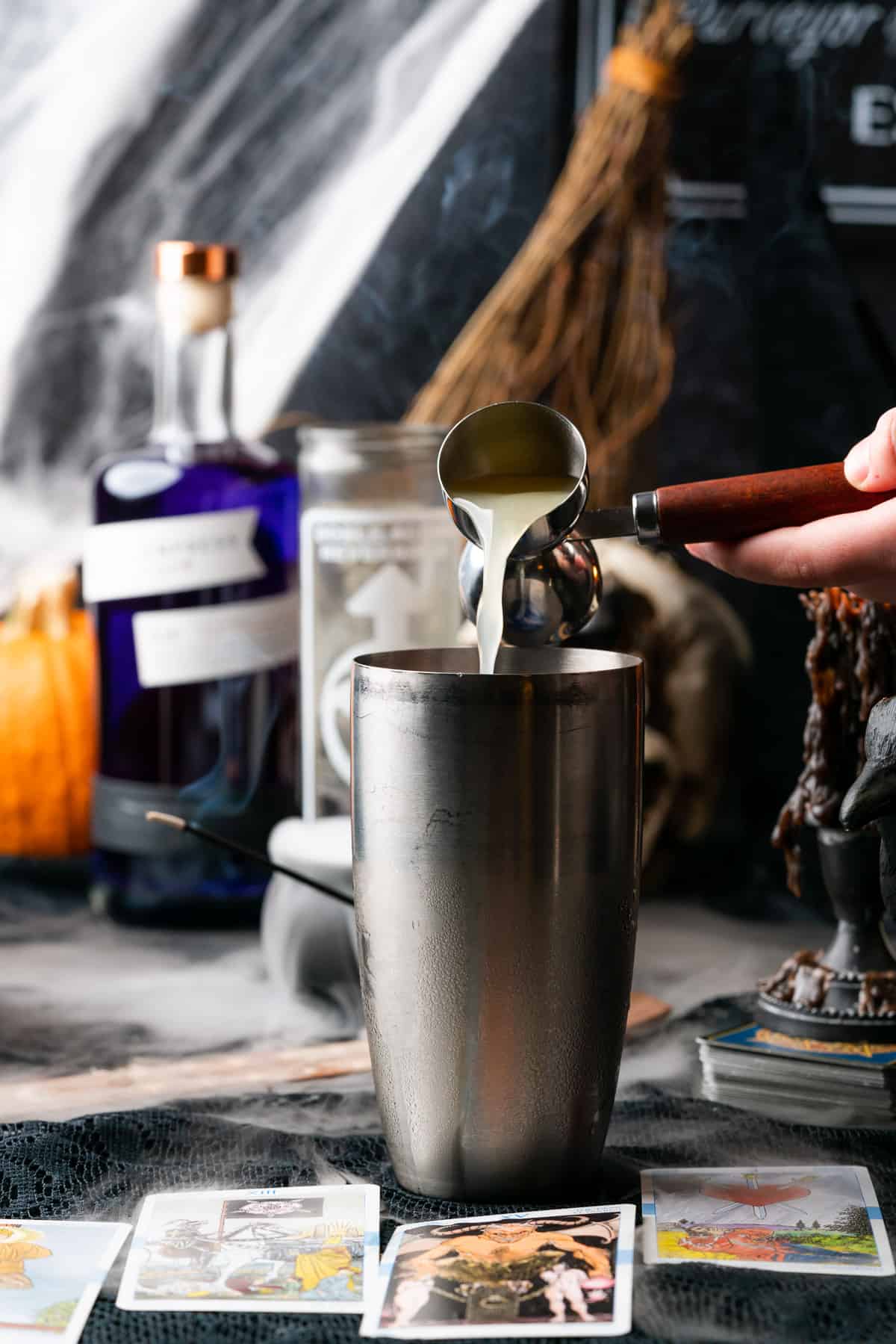 pouring lemon juice into a cocktail shaker with a spooky Halloween scene in the background 