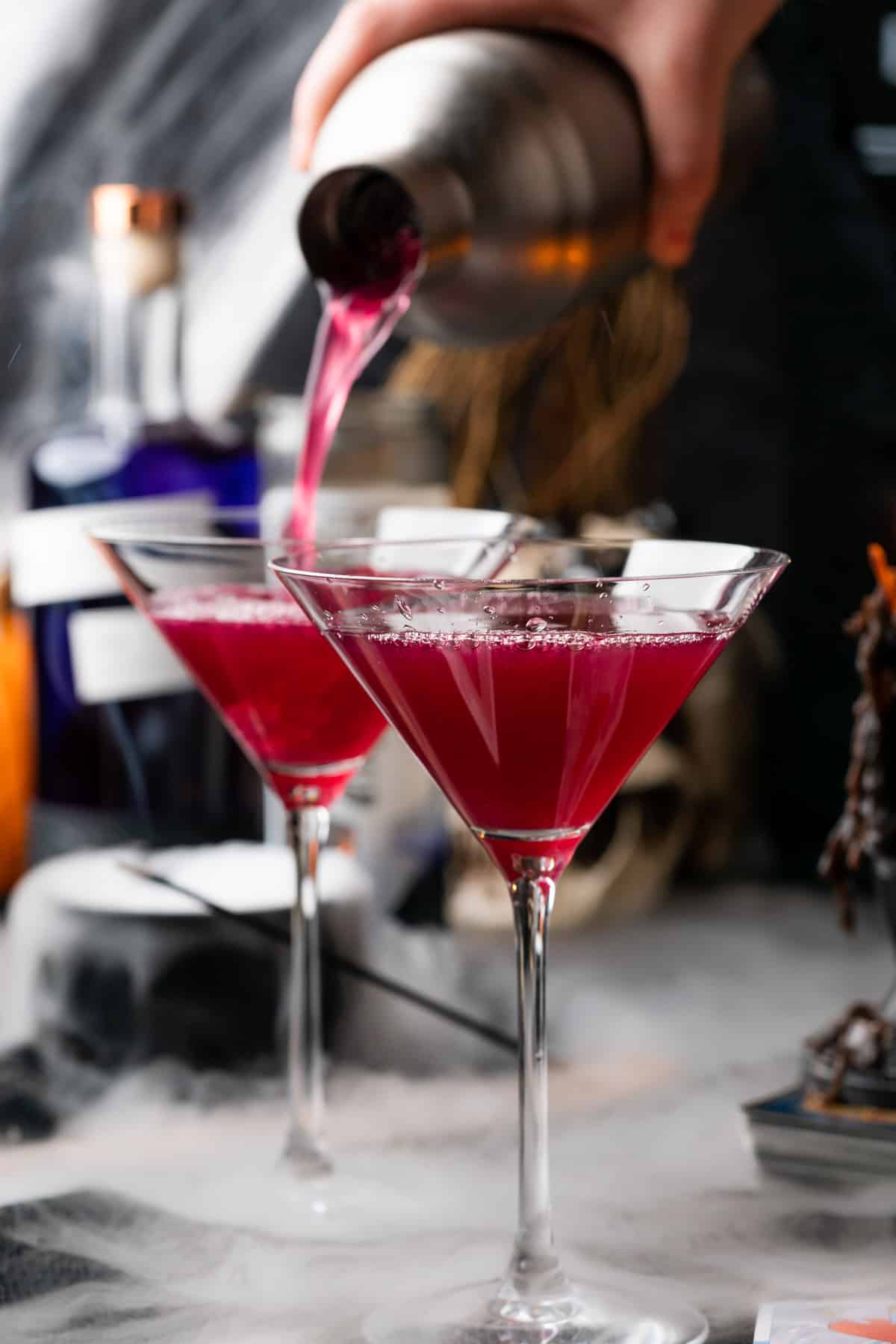 pouring purple cocktail liquid into a second martini glass 