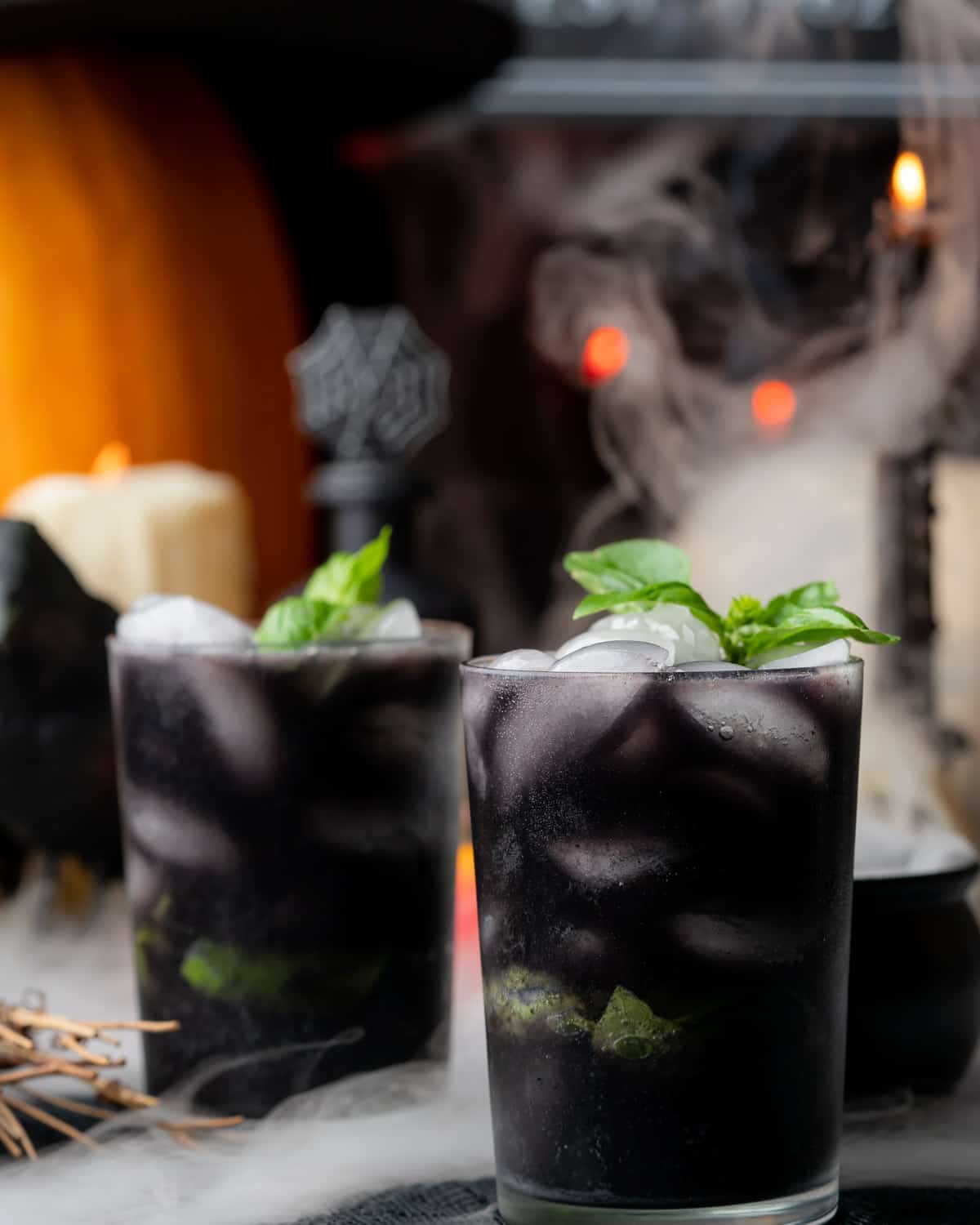 spooky blueberry basil gin cocktail with dry ice, pumpkins, candles and spiderwebs