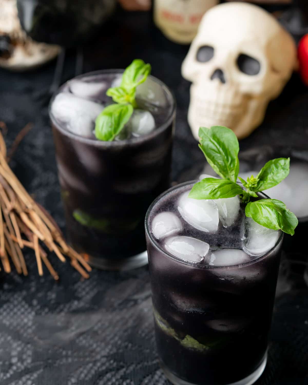 two black spooky blueberry gin cocktails with basil and skull in the background