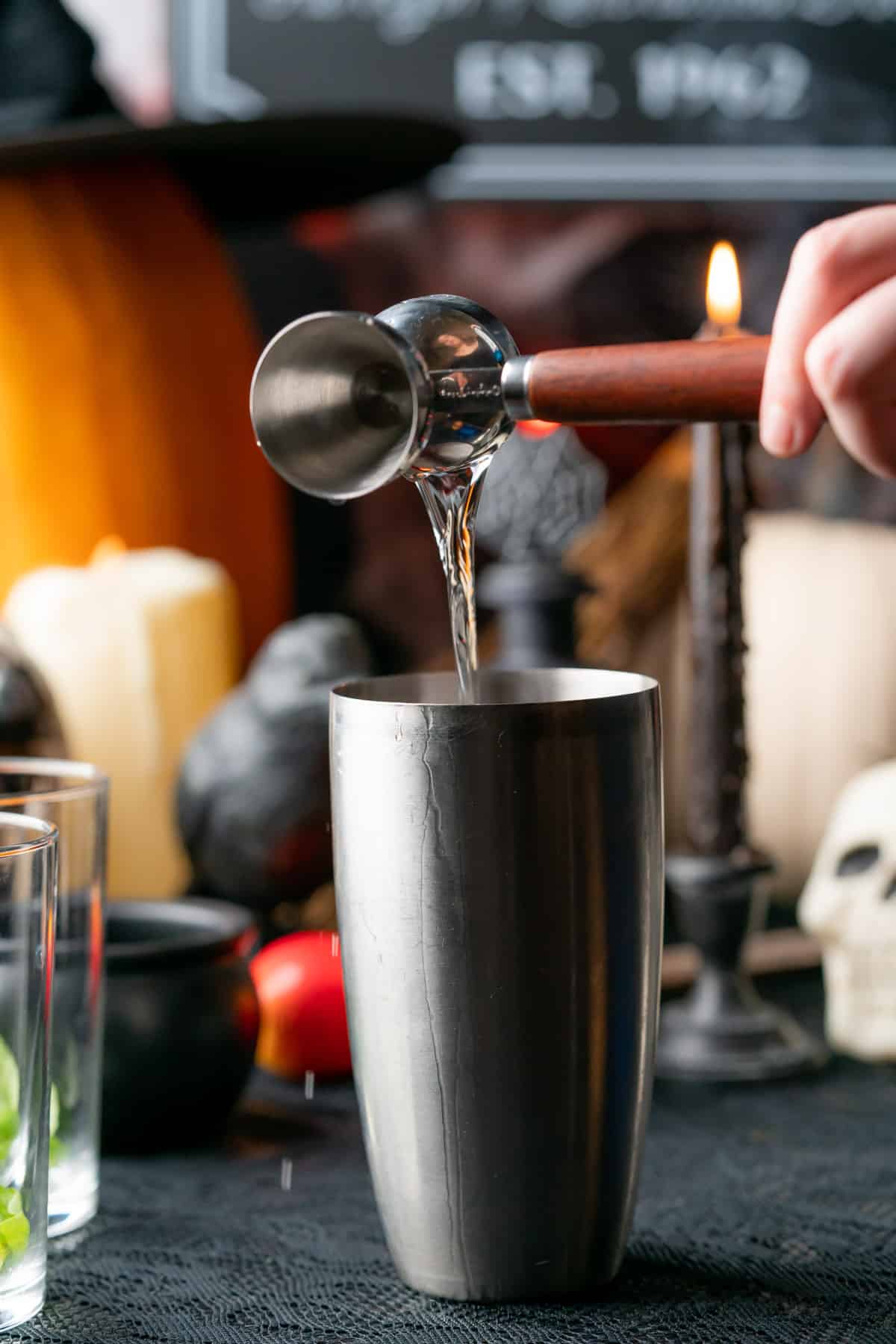 hand pouring in gin to a spooky cocktail with a creepy halloween scene in the background 