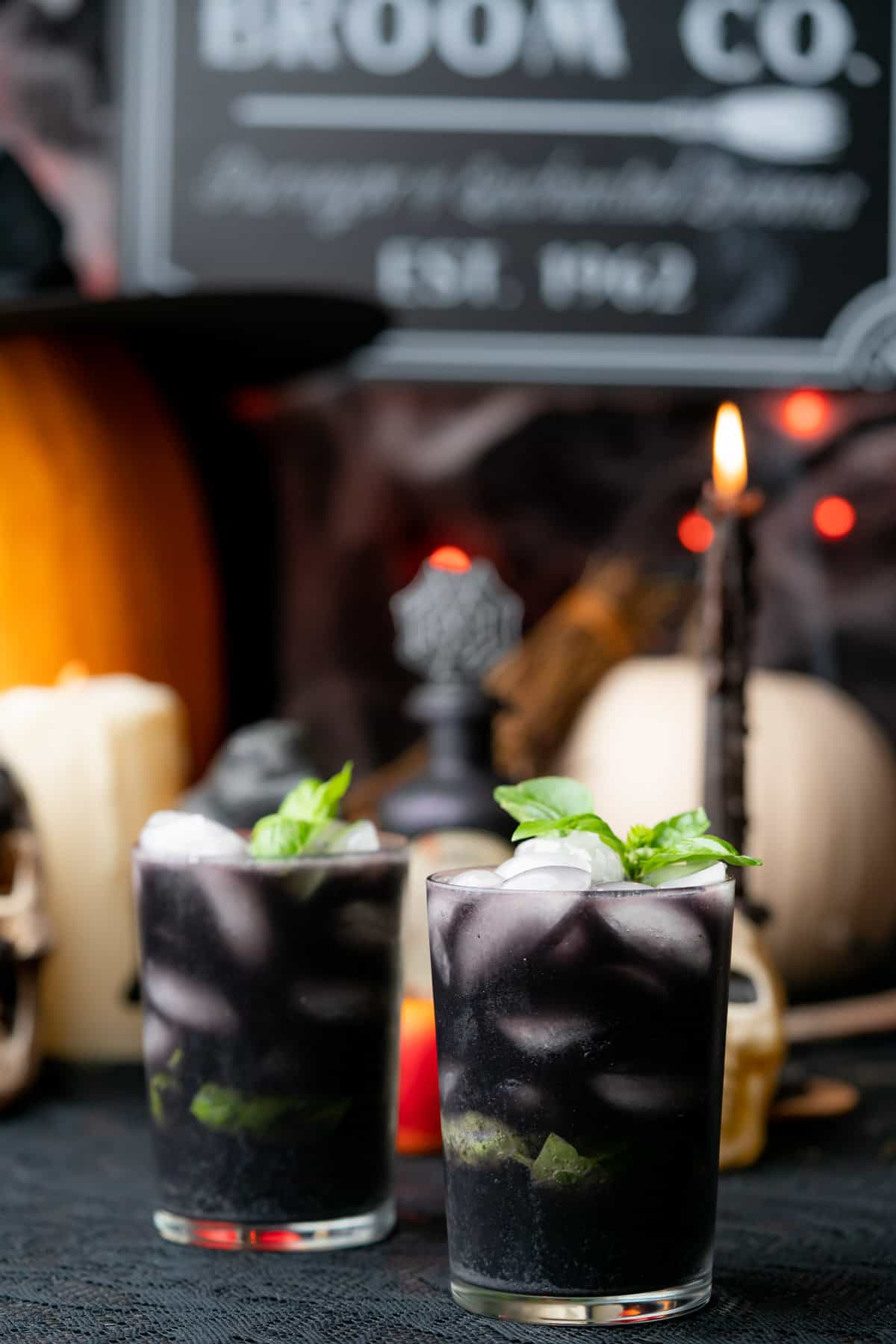 two large glasses of a black cocktail with a spooky halloween scene in the background