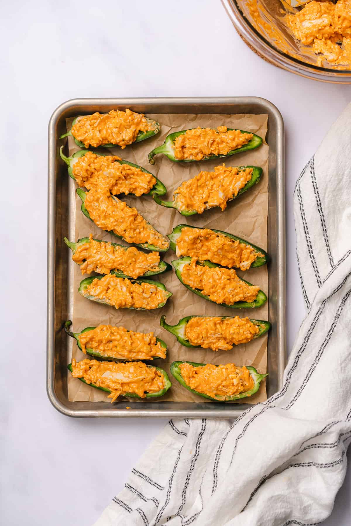 jalapeno halves filled with buffalo chicken mixture on a parchment lined baking sheet