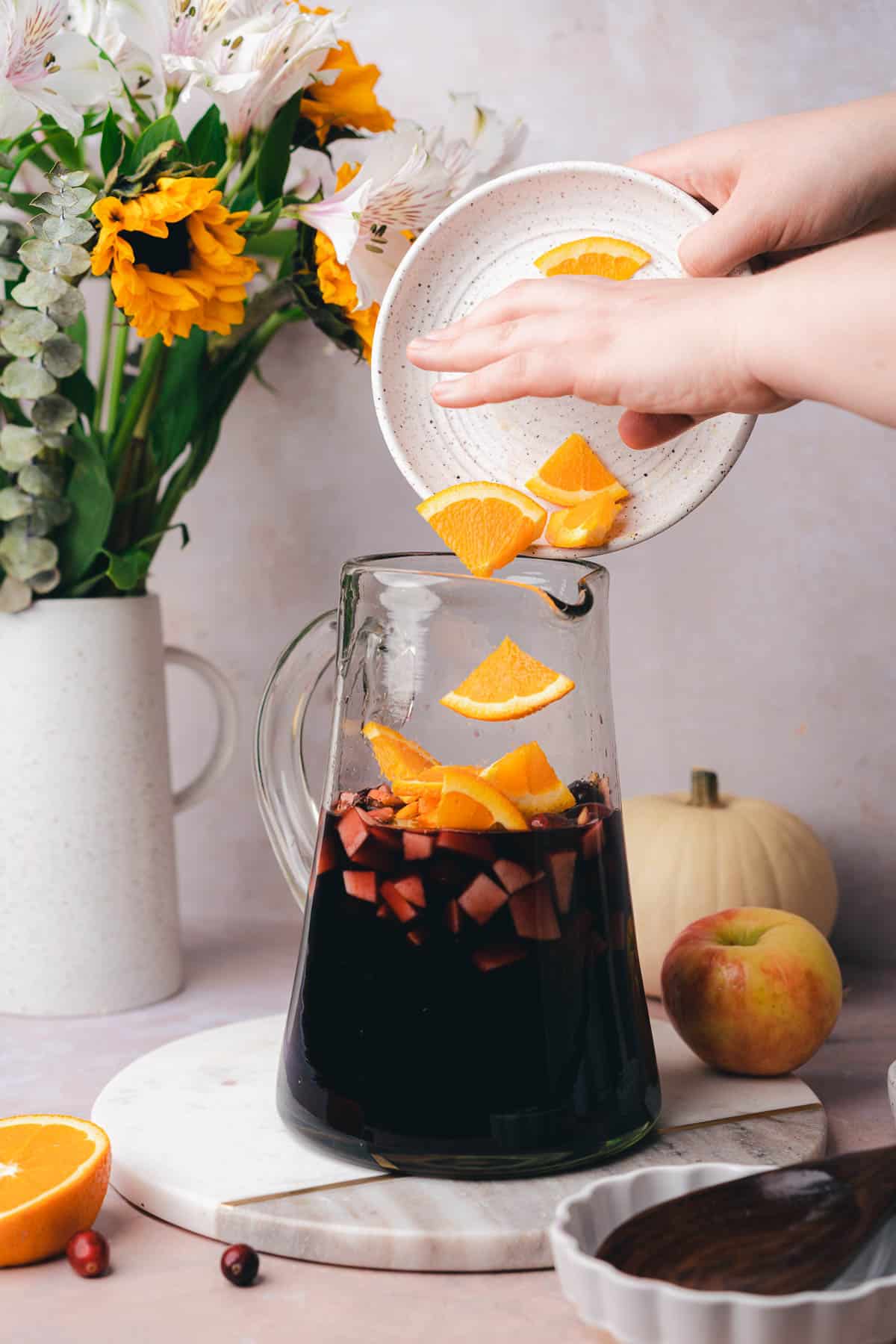 hand dropping in orange slices to a sangria pitcher 