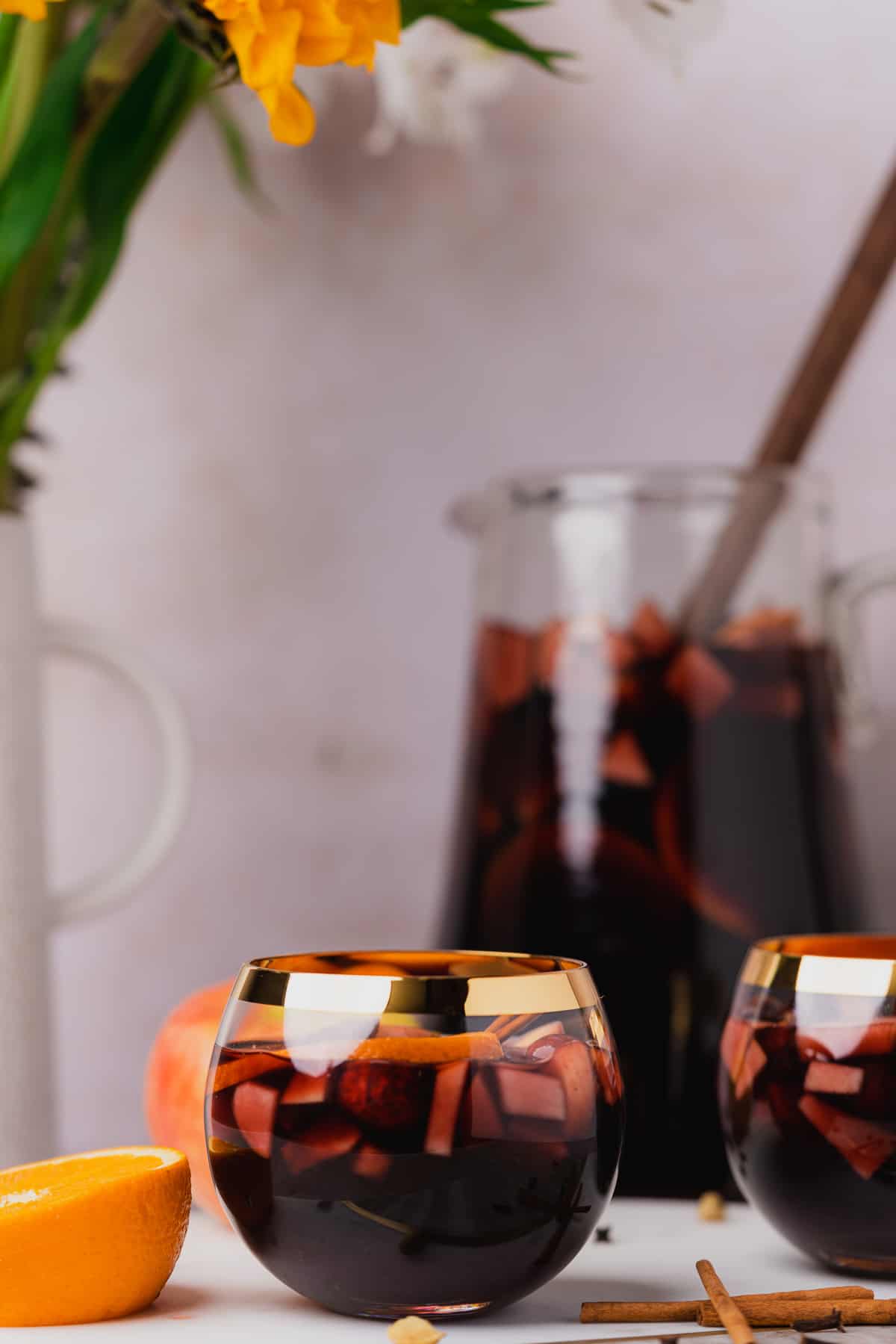 two goblet glasses with red wine whiskey sangria and a large pitcher in the background